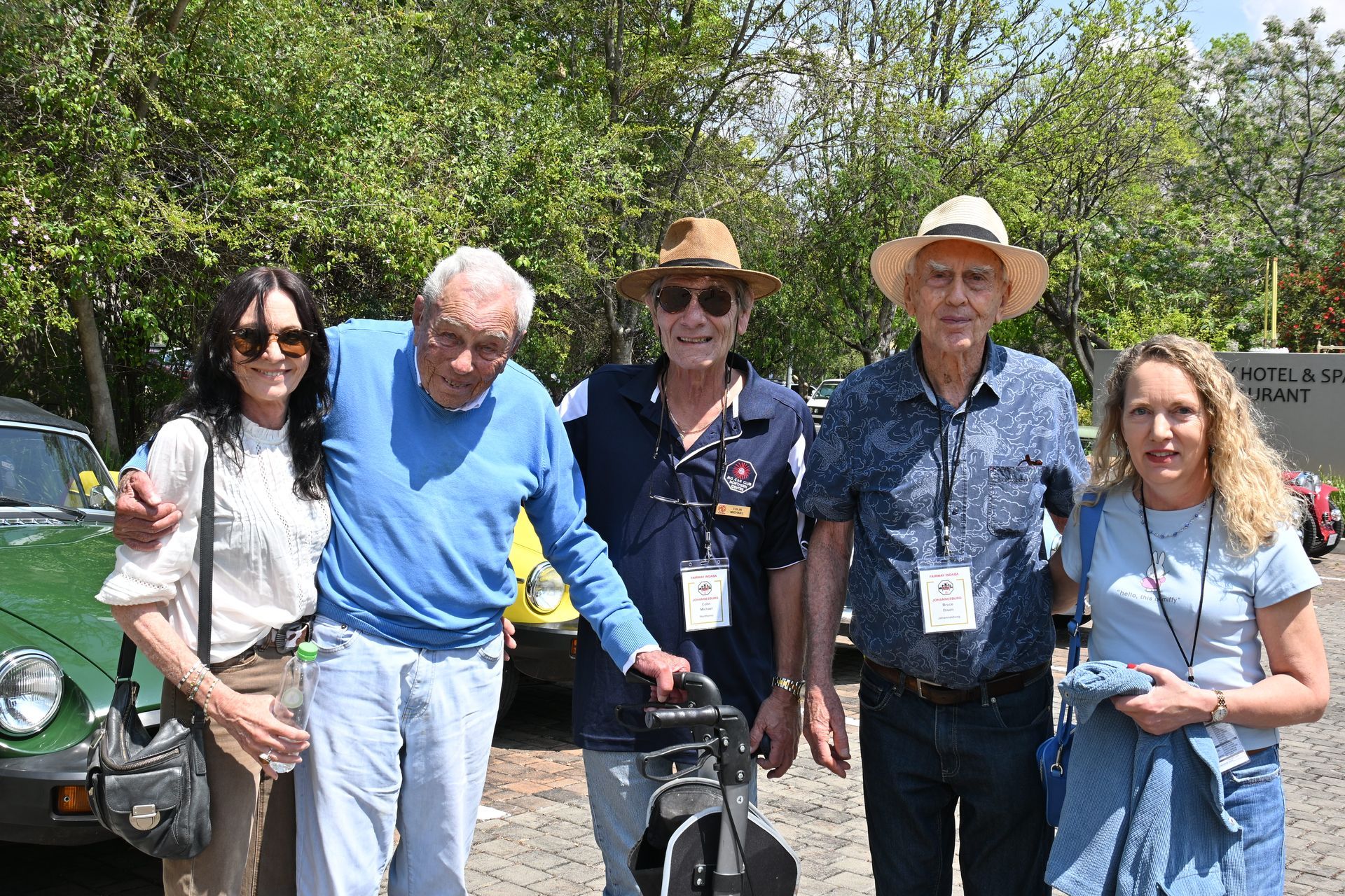 Five adults standing outdoors in a sunny park, smiling beside a bicycle.