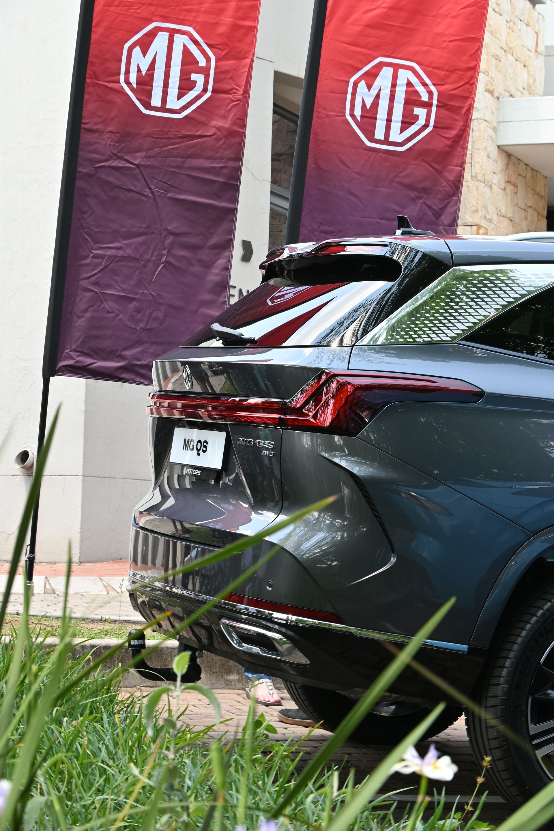 Rear view of a dark SUV at an MG event, with red MG banners and grass in the foreground