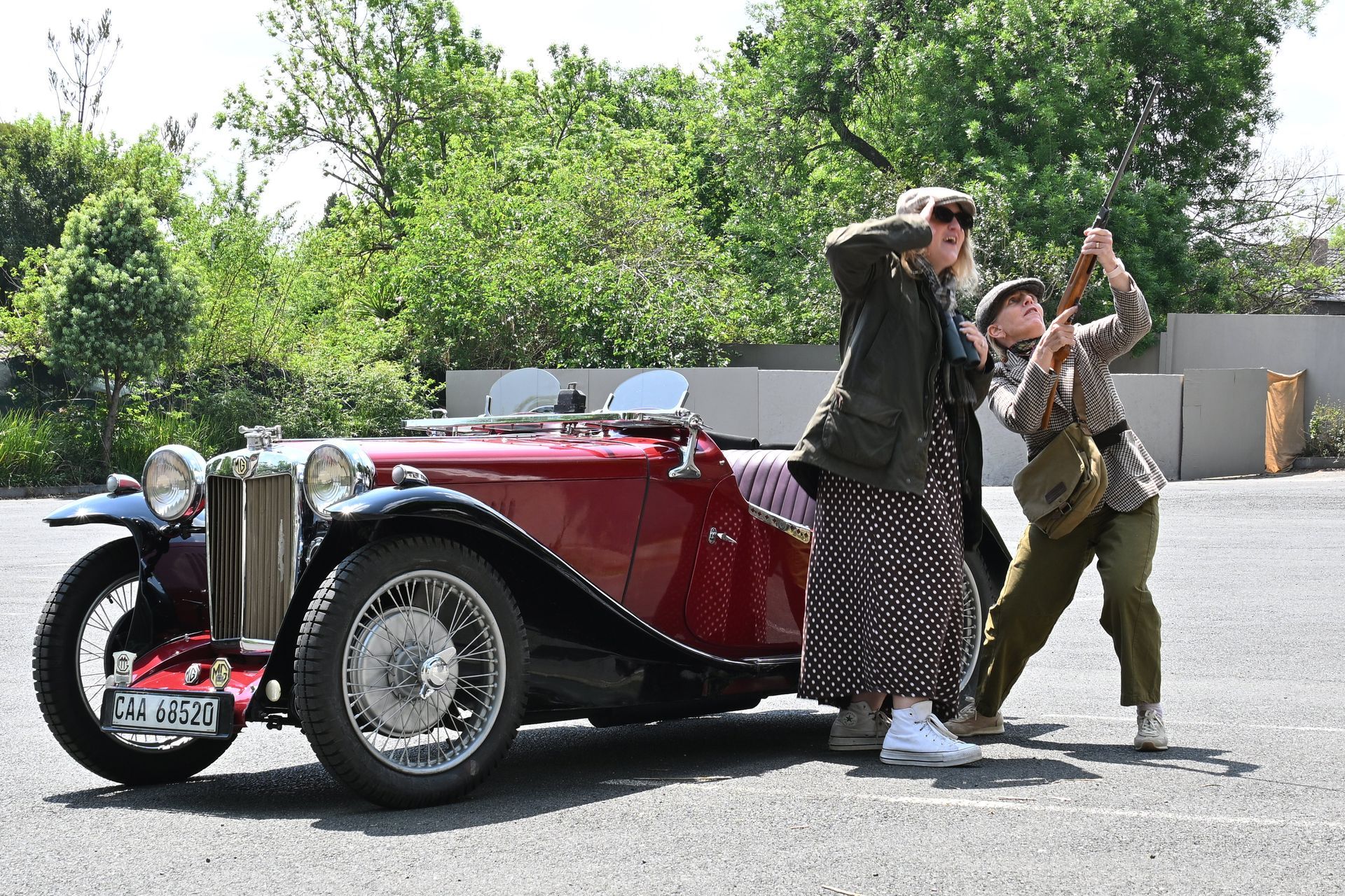 Two people posing beside a red vintage convertible on a sunny roadside