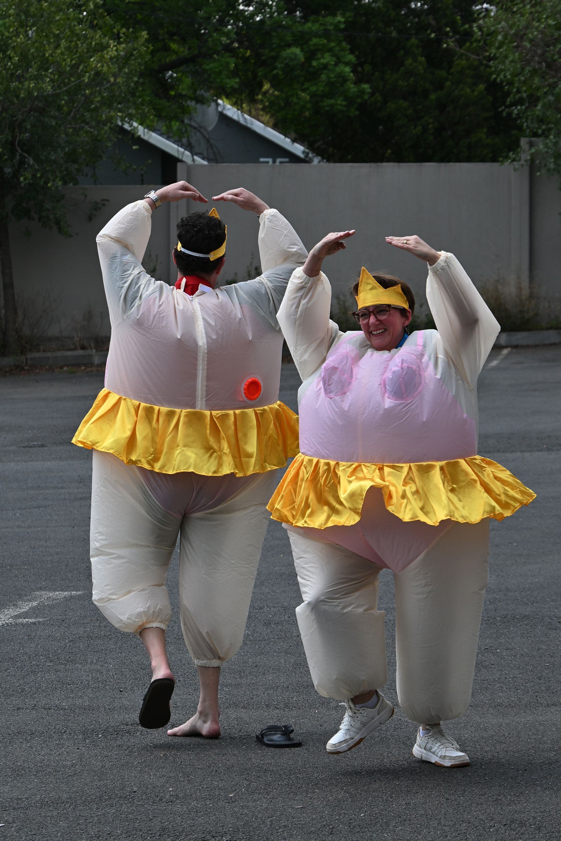 Two people in white and yellow costumes dancing outdoors in a parking lot.