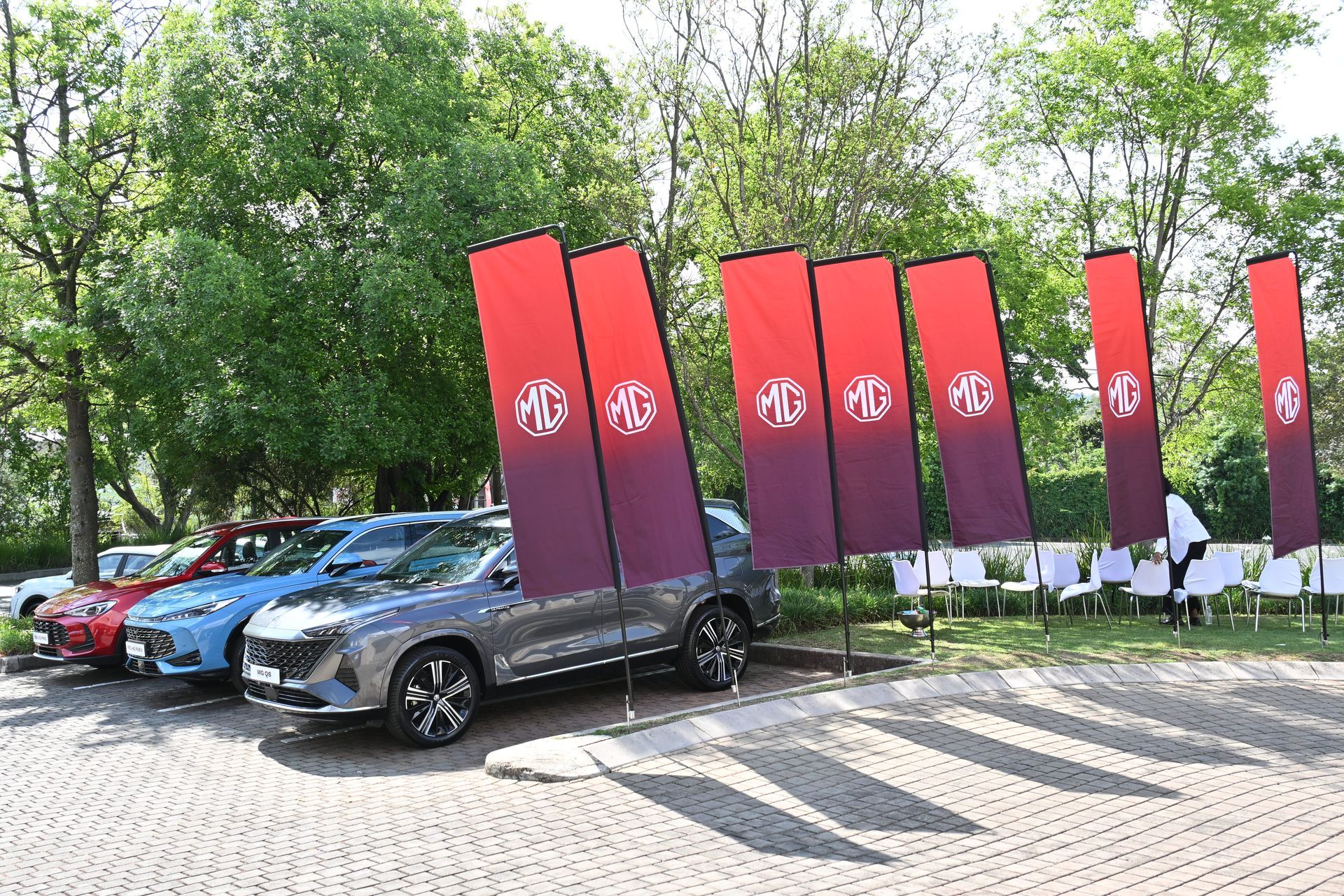 Red and black cars parked beside tall red banners in a tree-lined lot.