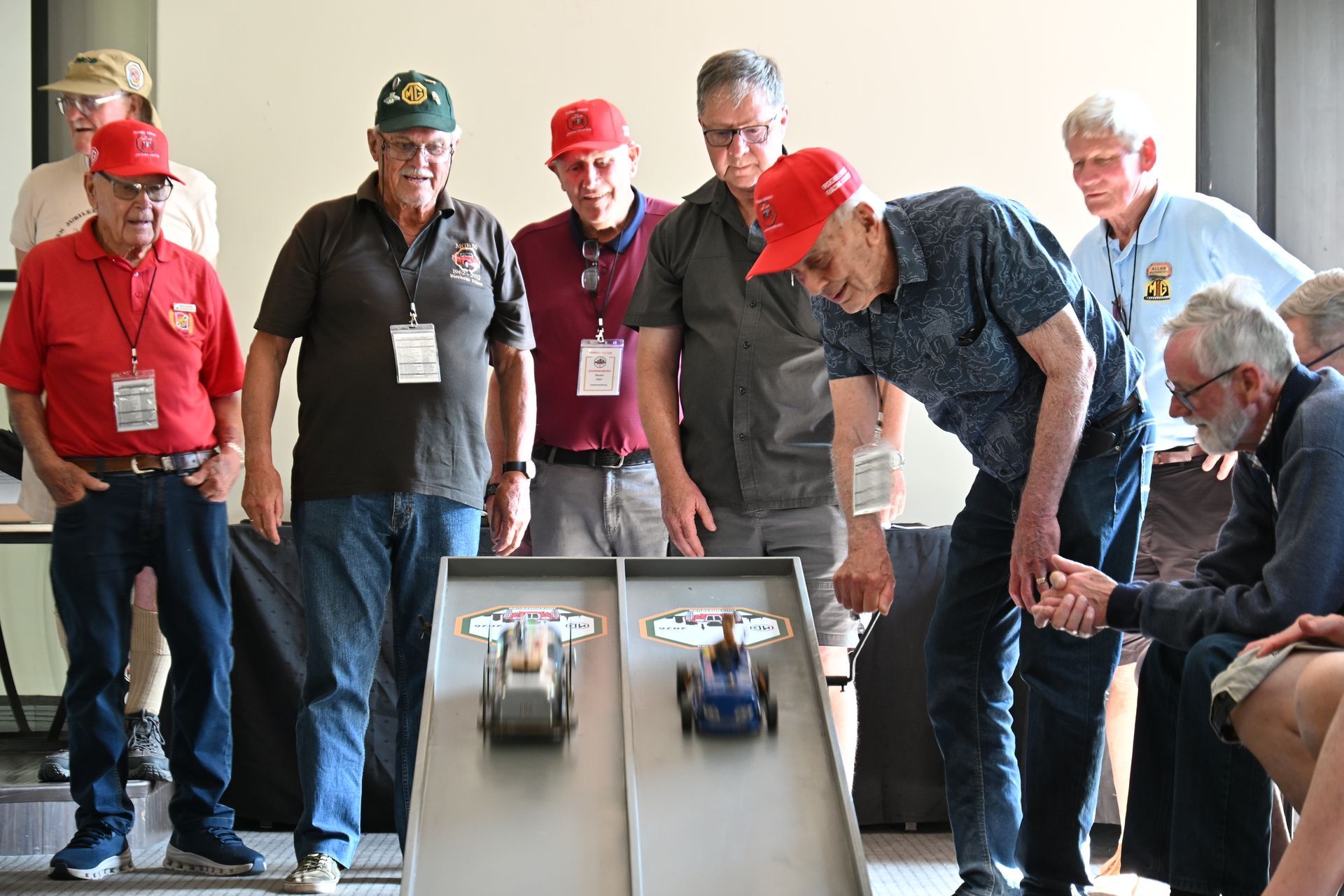 People watching two toy cars race down a ramp indoors