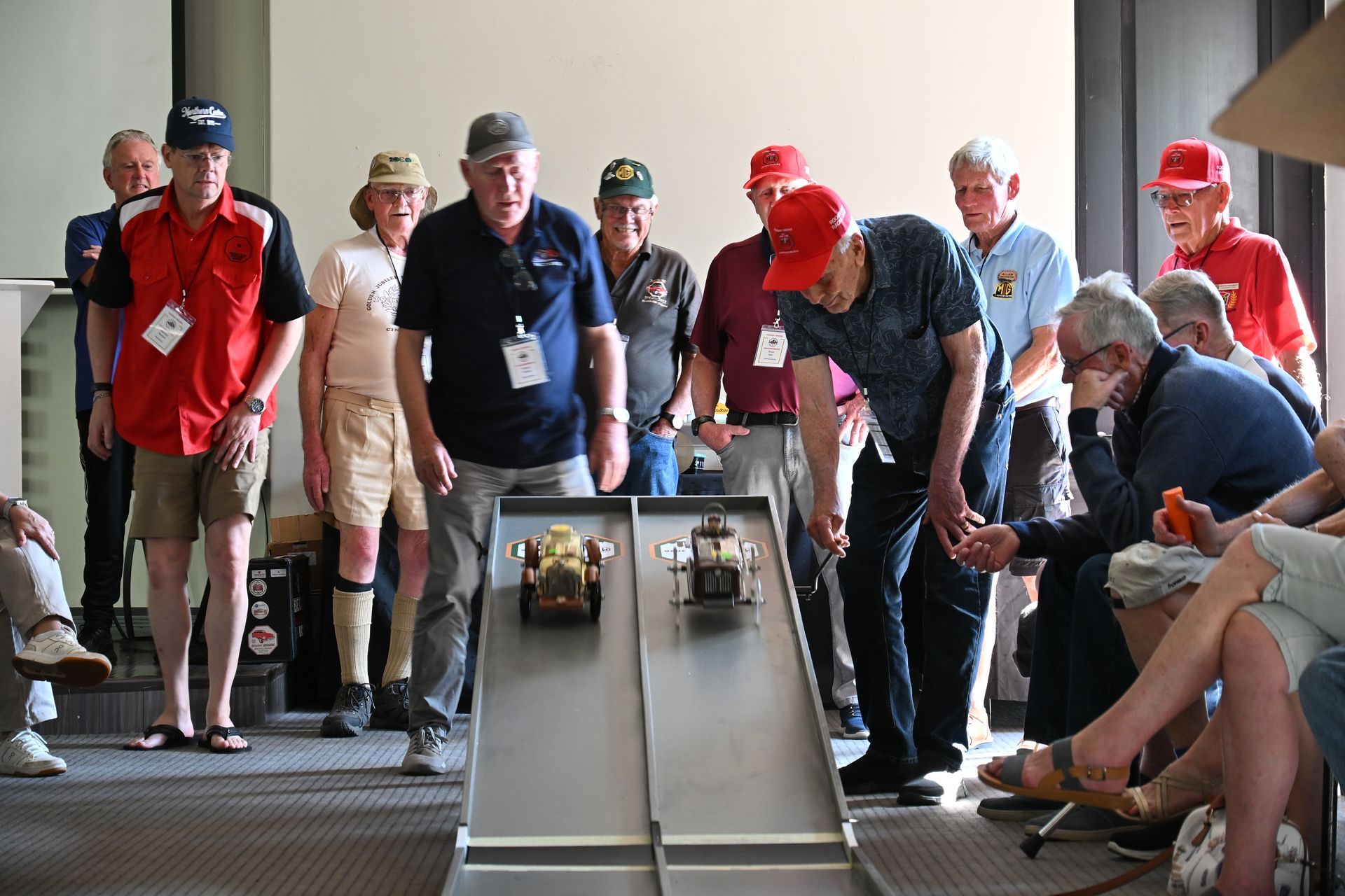 People watching a tabletop marble race, leaning over lanes in a bright indoor hall