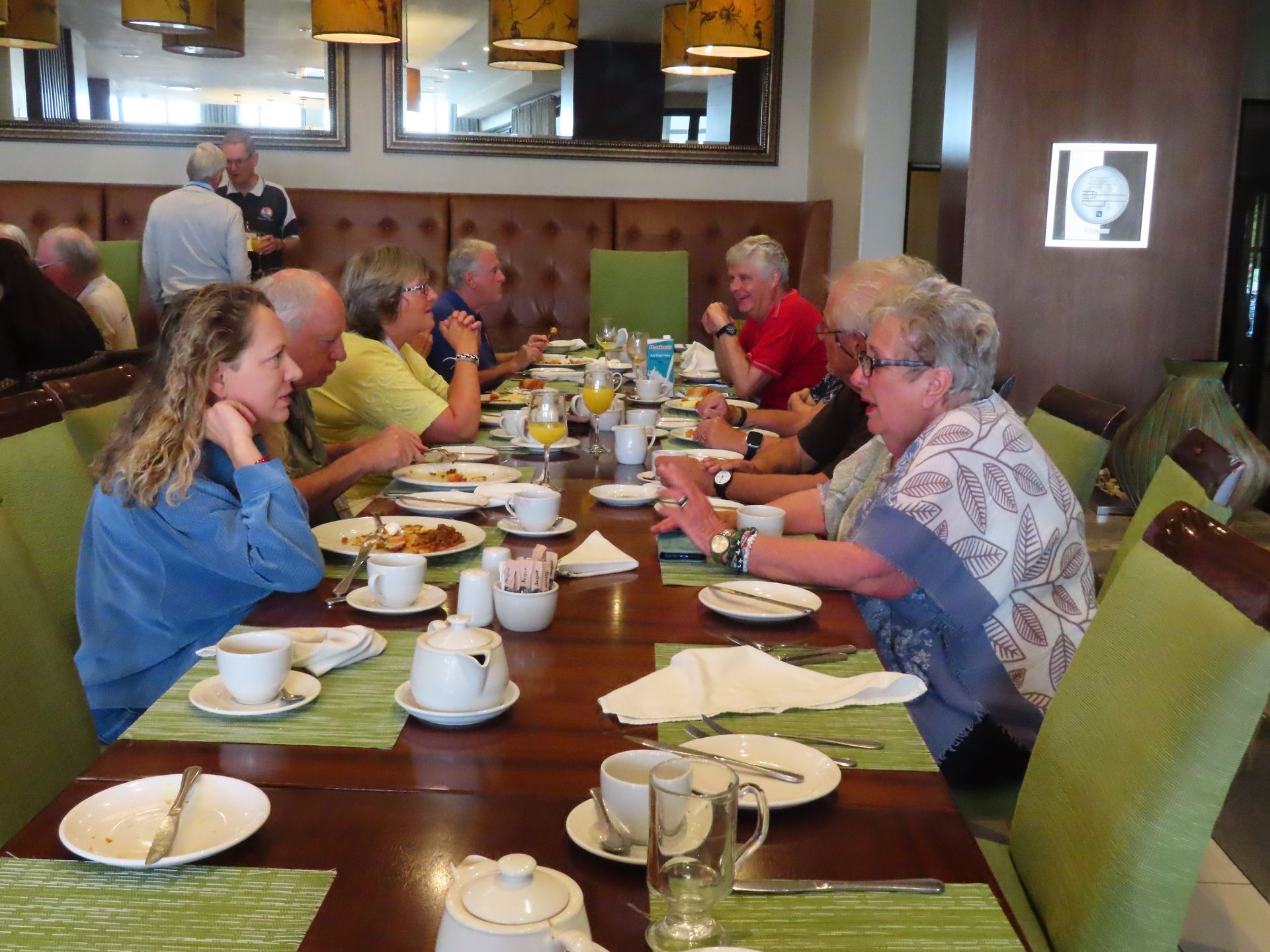 People seated at a dining table in a restaurant, eating and talking over plates and cups.