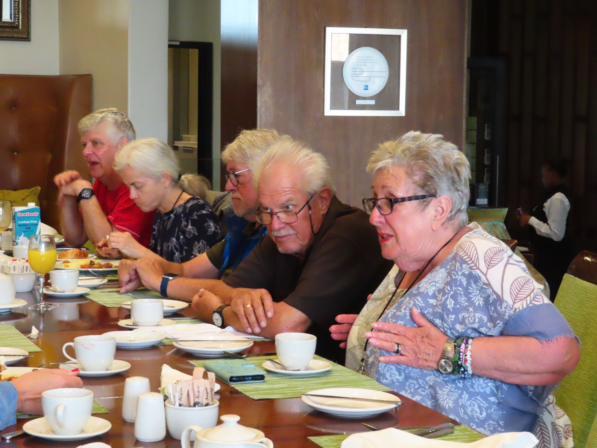 People seated at a long table in a dining room, eating and talking during a meal