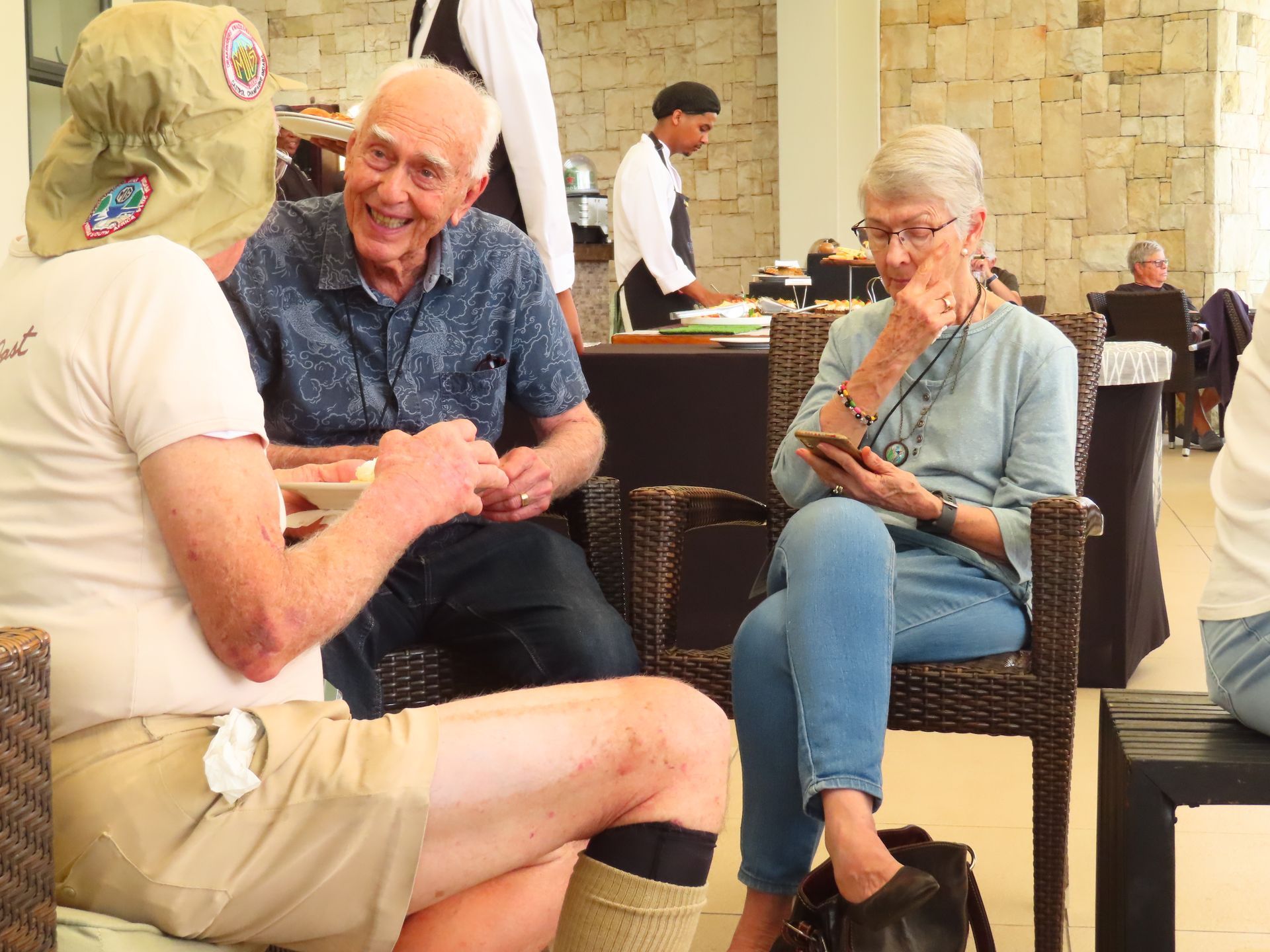 People sitting and chatting in a casual indoor lounge with wicker chairs and a stone wall.