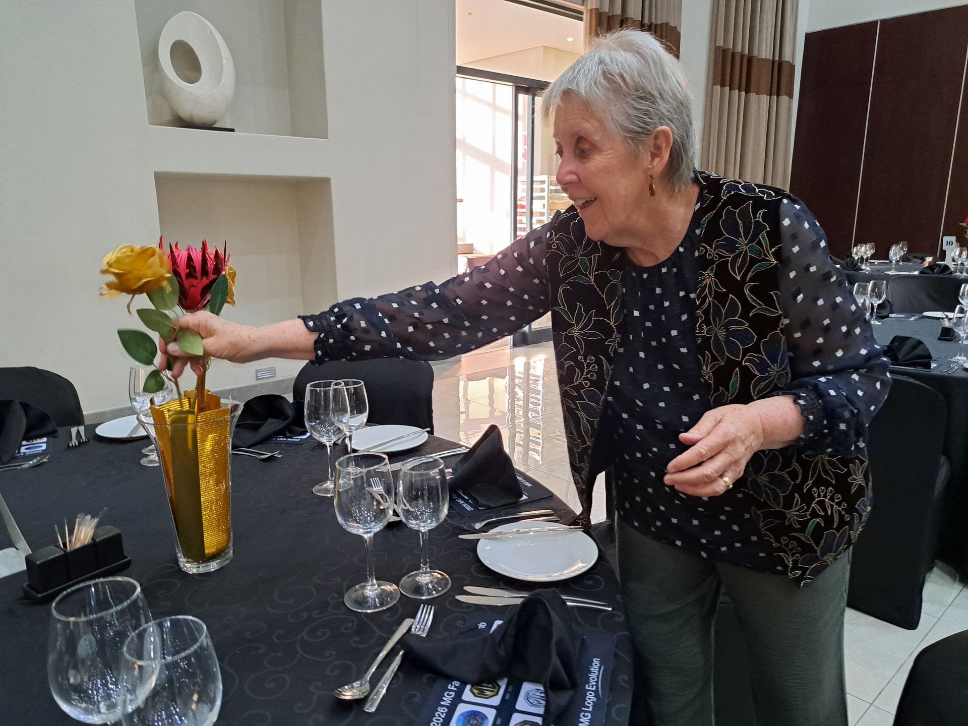 Woman arranging flowers on a dining table in a bright room