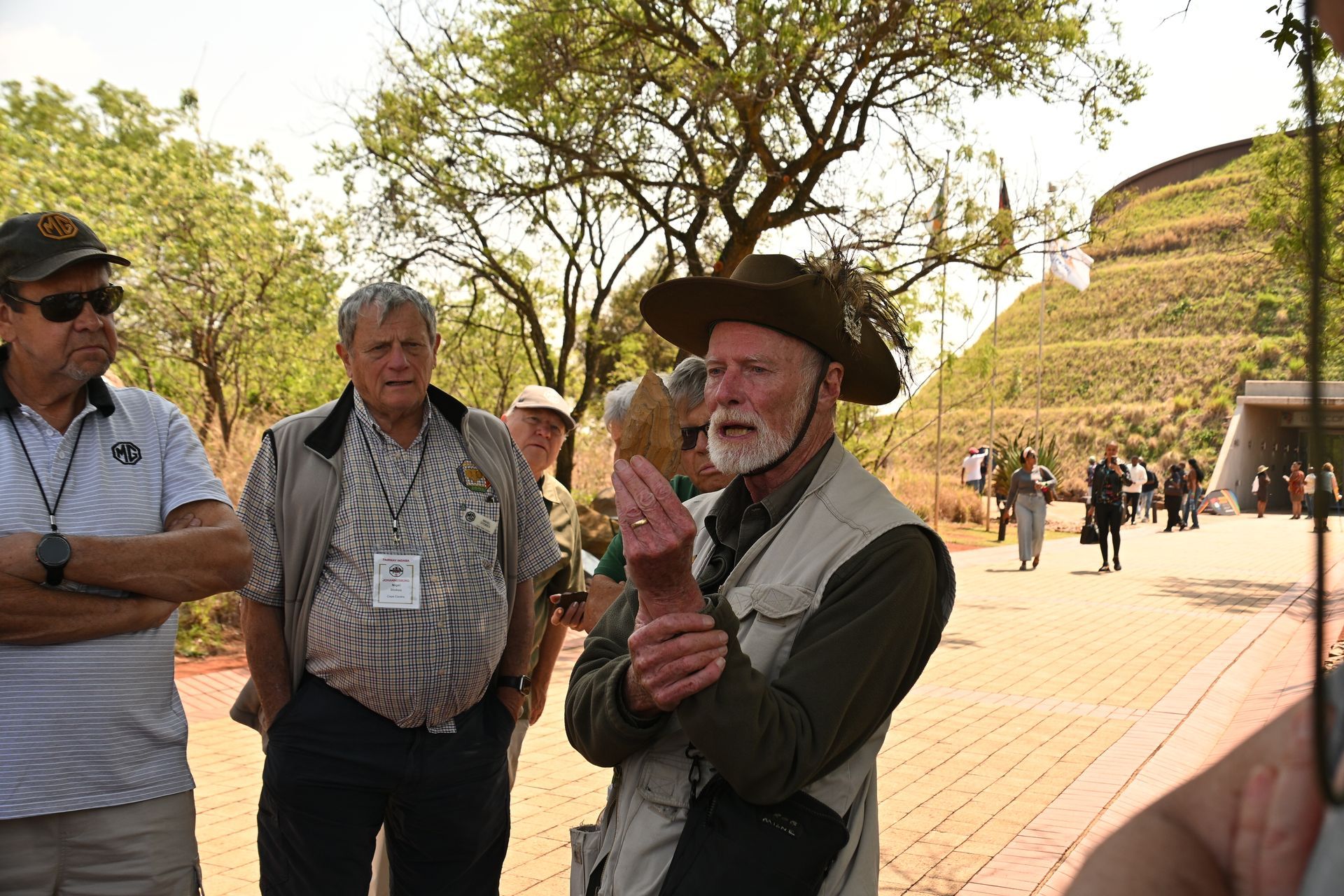 Tour guide in a brown hat speaking to a group at an outdoor historical site.