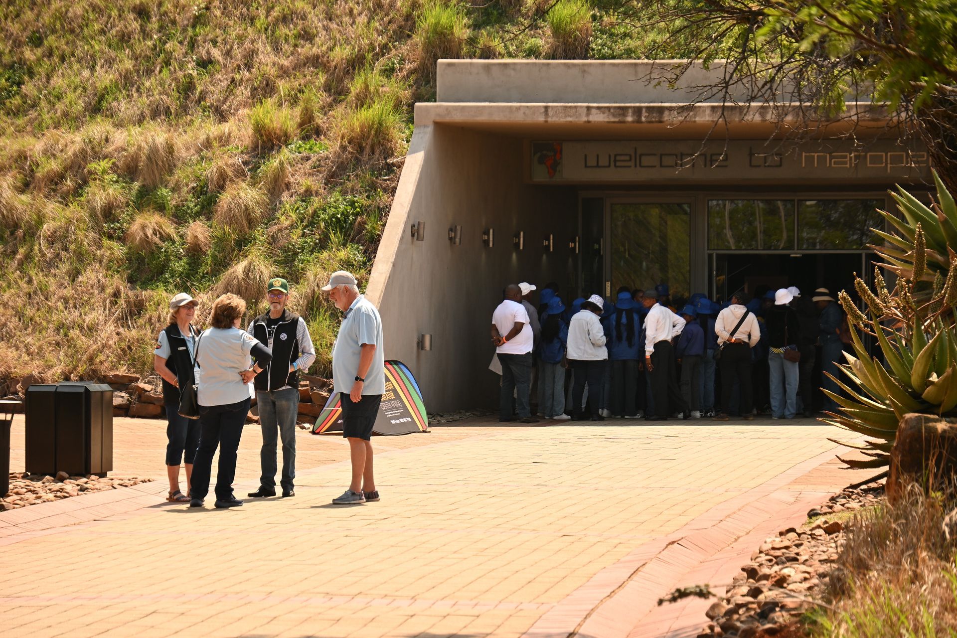 People gathered at the entrance of a concrete building on a sunny hillside walkway