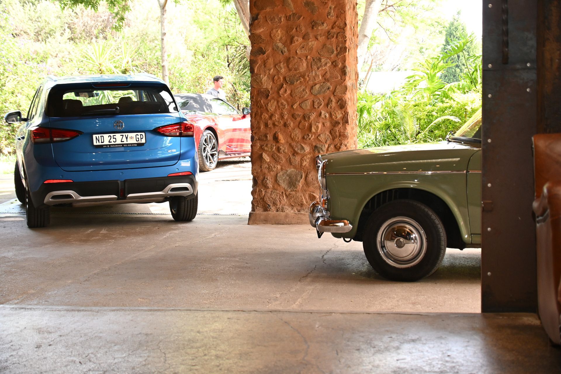 Blue SUV and green truck parked under a covered driveway with trees in the background