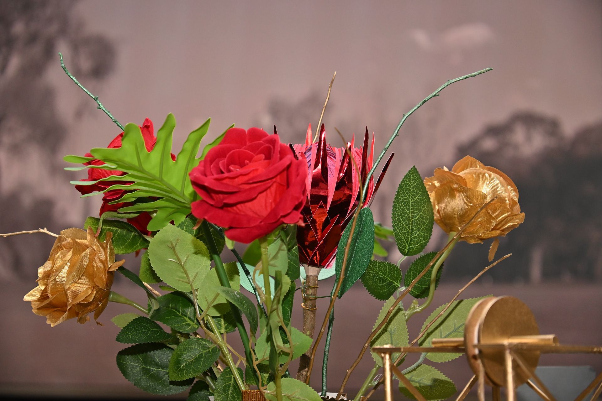 Colorful floral arrangement with red, gold, and green flowers on a table against a blurred background