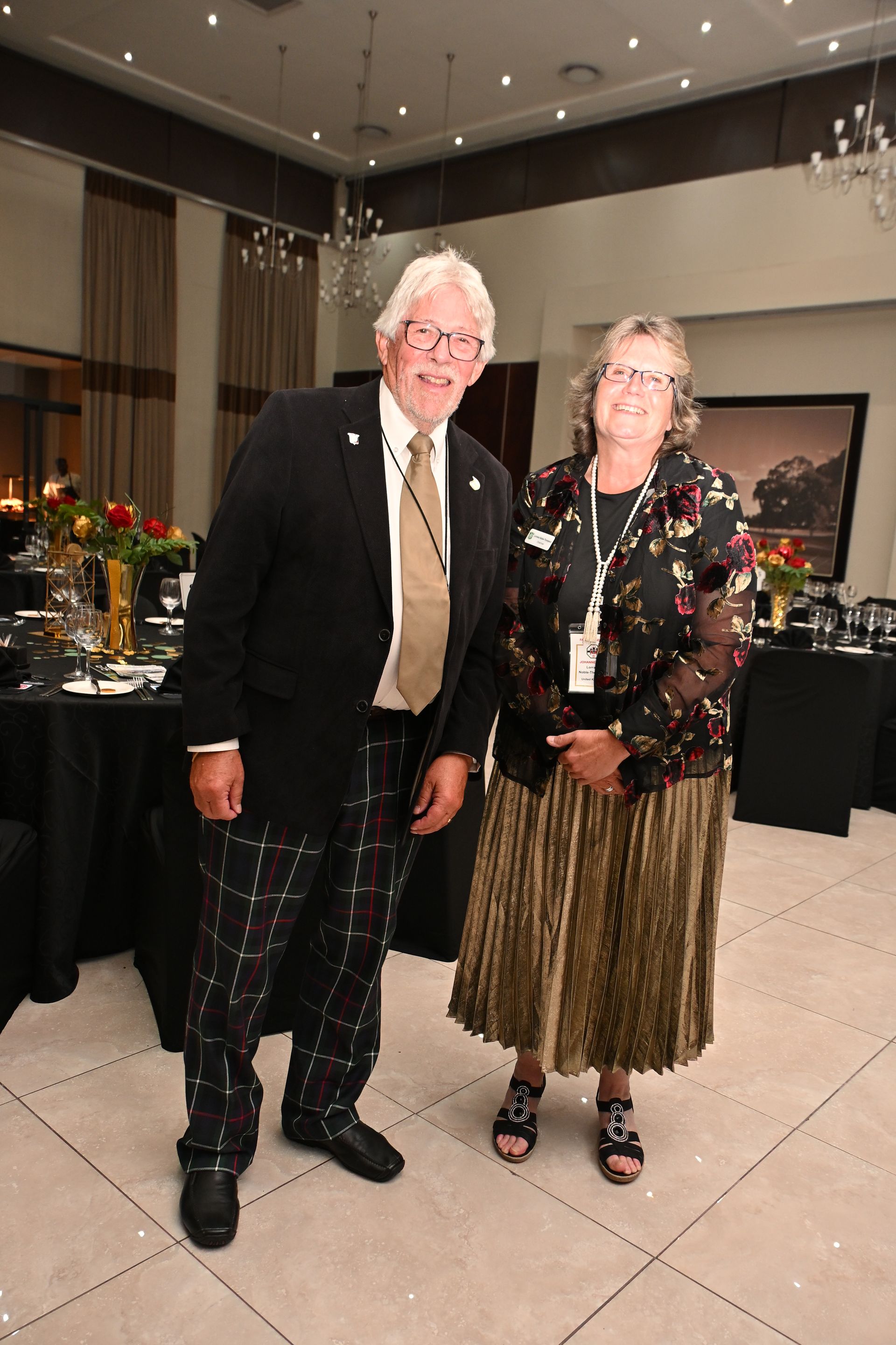 Two people standing together at a formal indoor event, dressed in semi-formal attire, smiling.