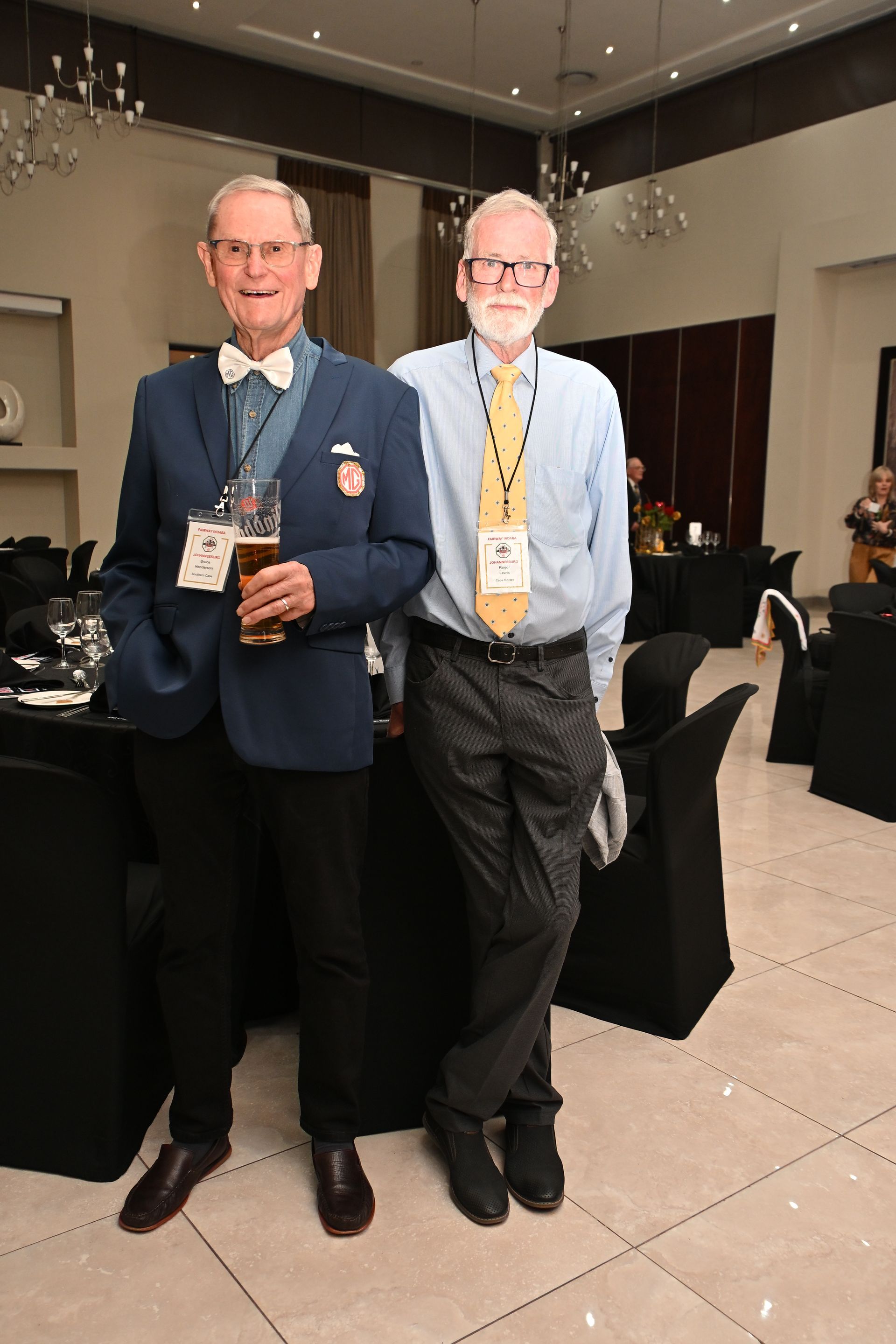 Two men posing at a formal event in a conference hall, wearing badges and blazers.