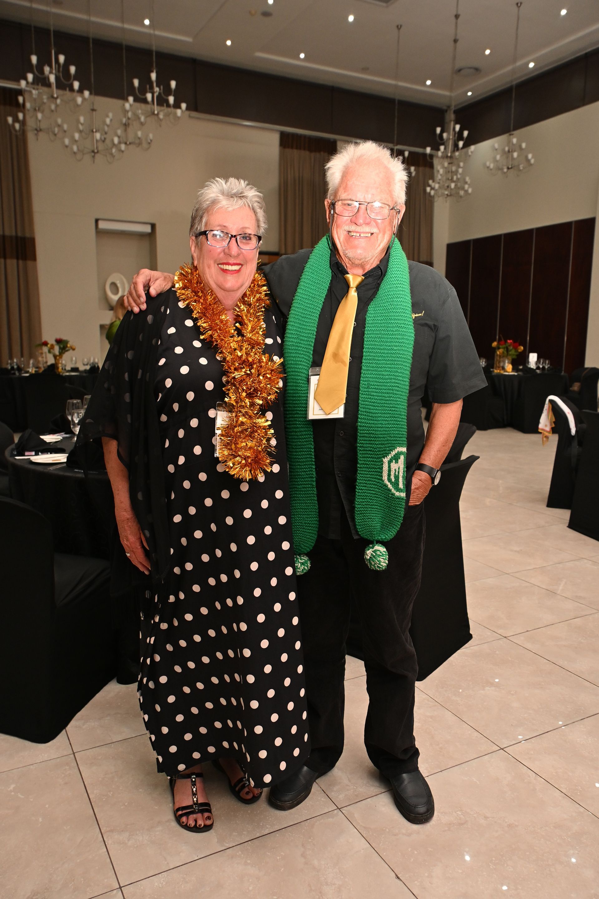 Two people in festive garlands pose smiling in a banquet hall.