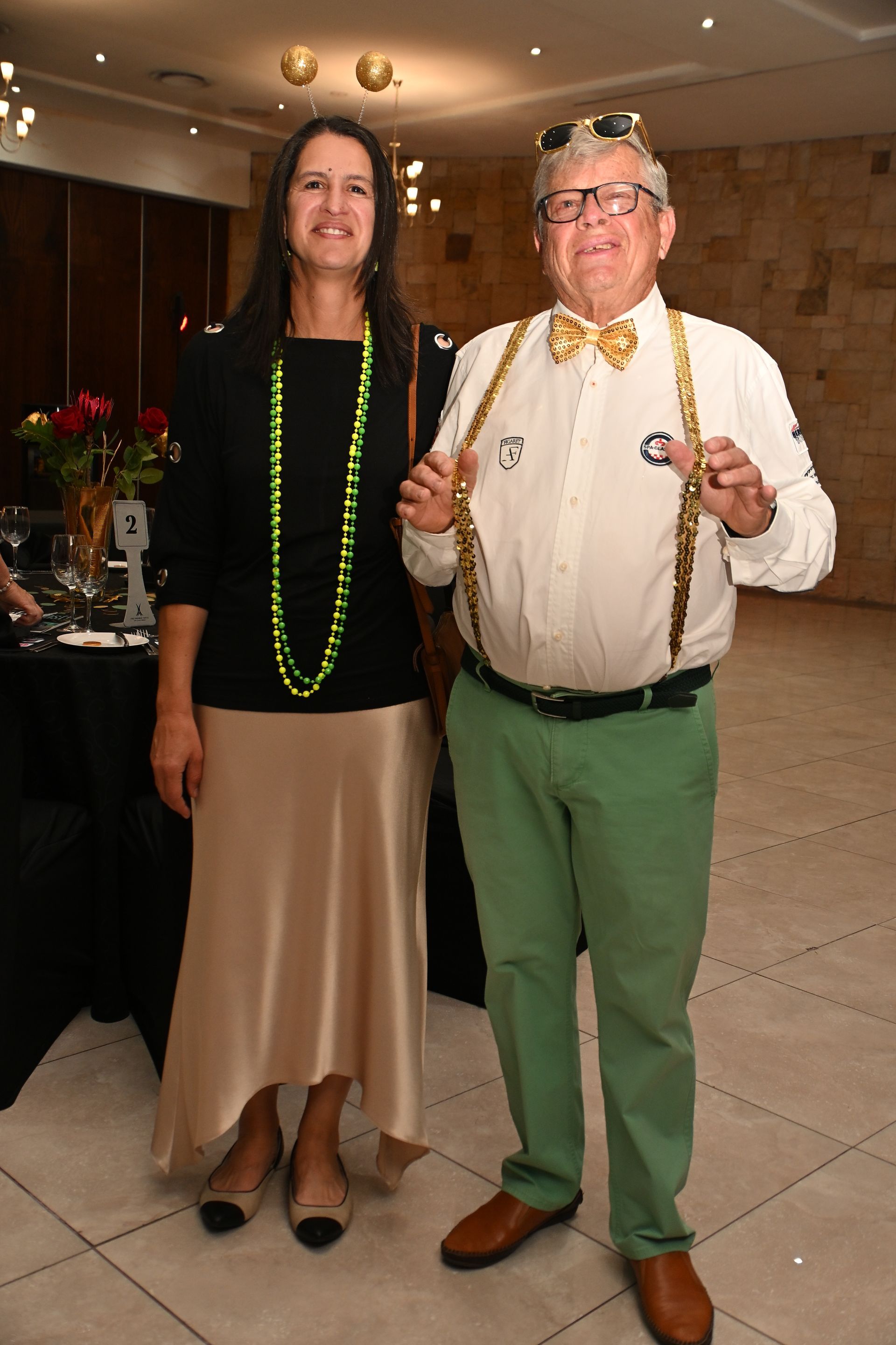 Two people posing indoors, wearing lei necklaces and smiling at the camera.