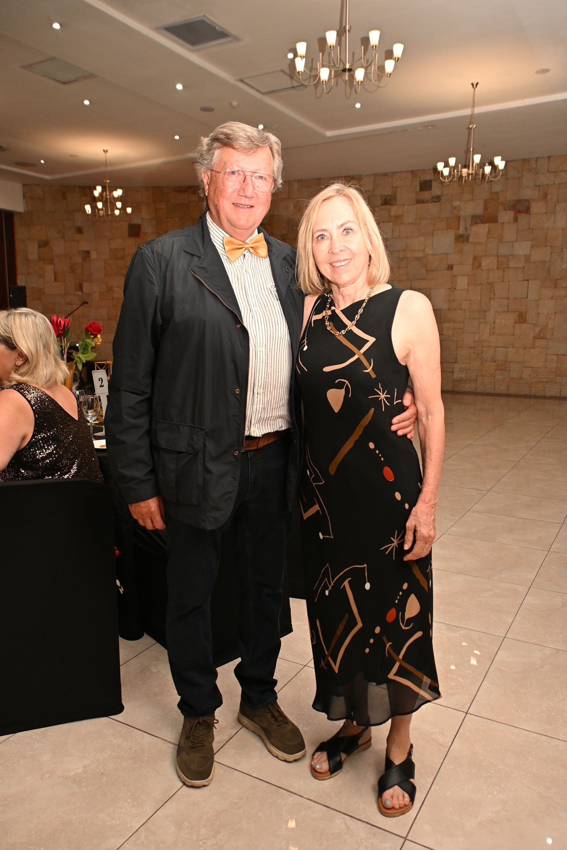 Two people standing together at a formal event, wearing black attire in a banquet hall.