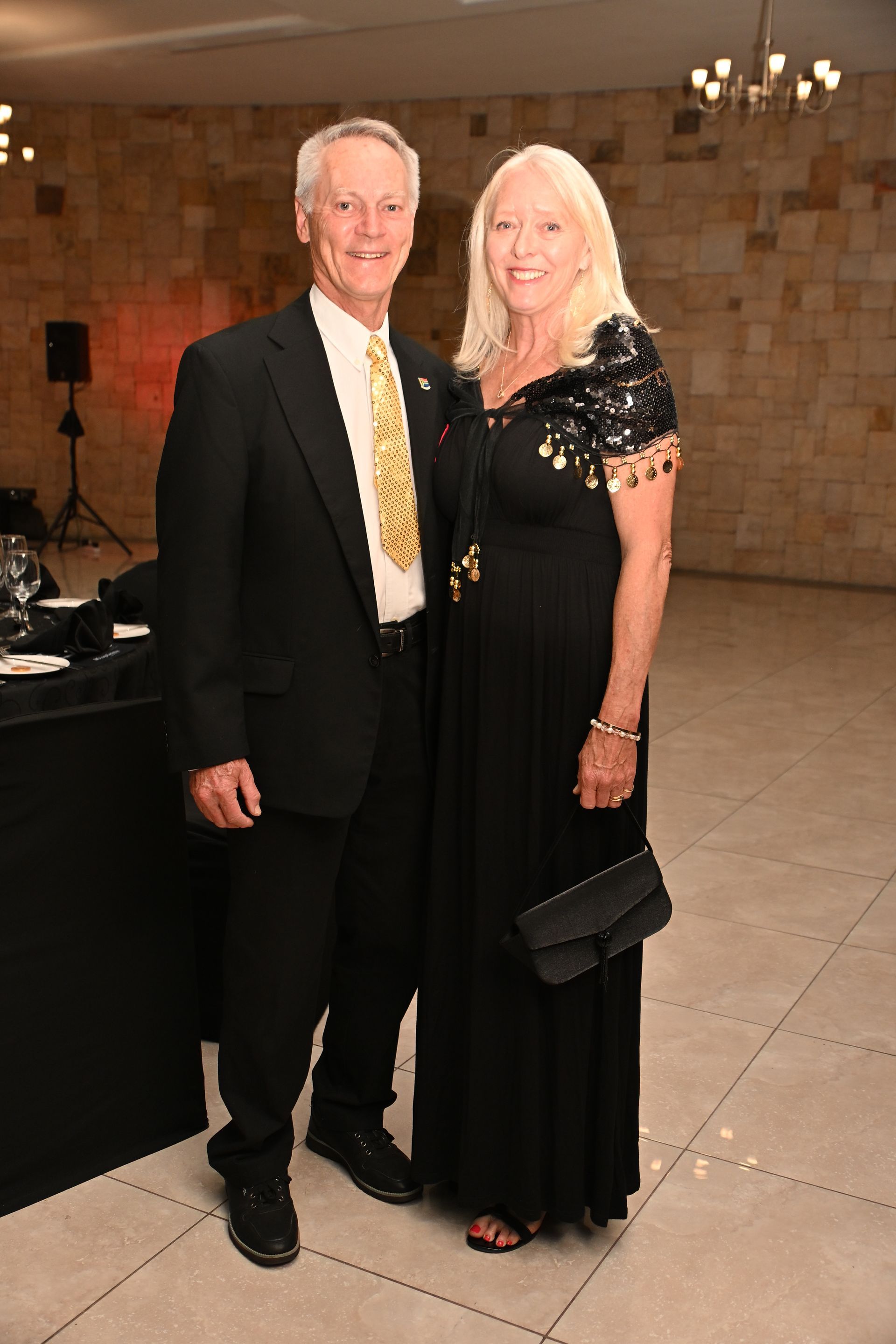 Two people in formal attire pose together in a warmly lit hall.
