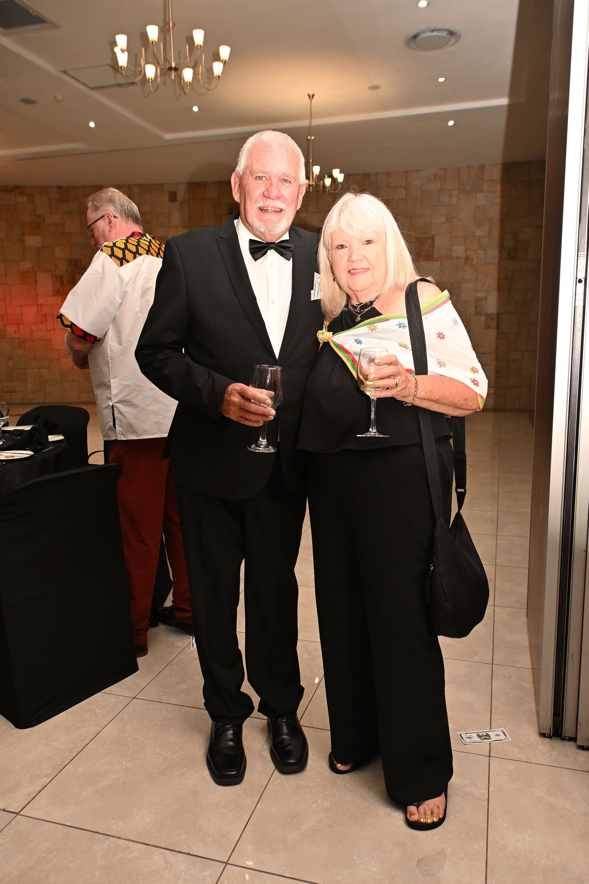 Two people in formal wear holding drinks at an indoor event