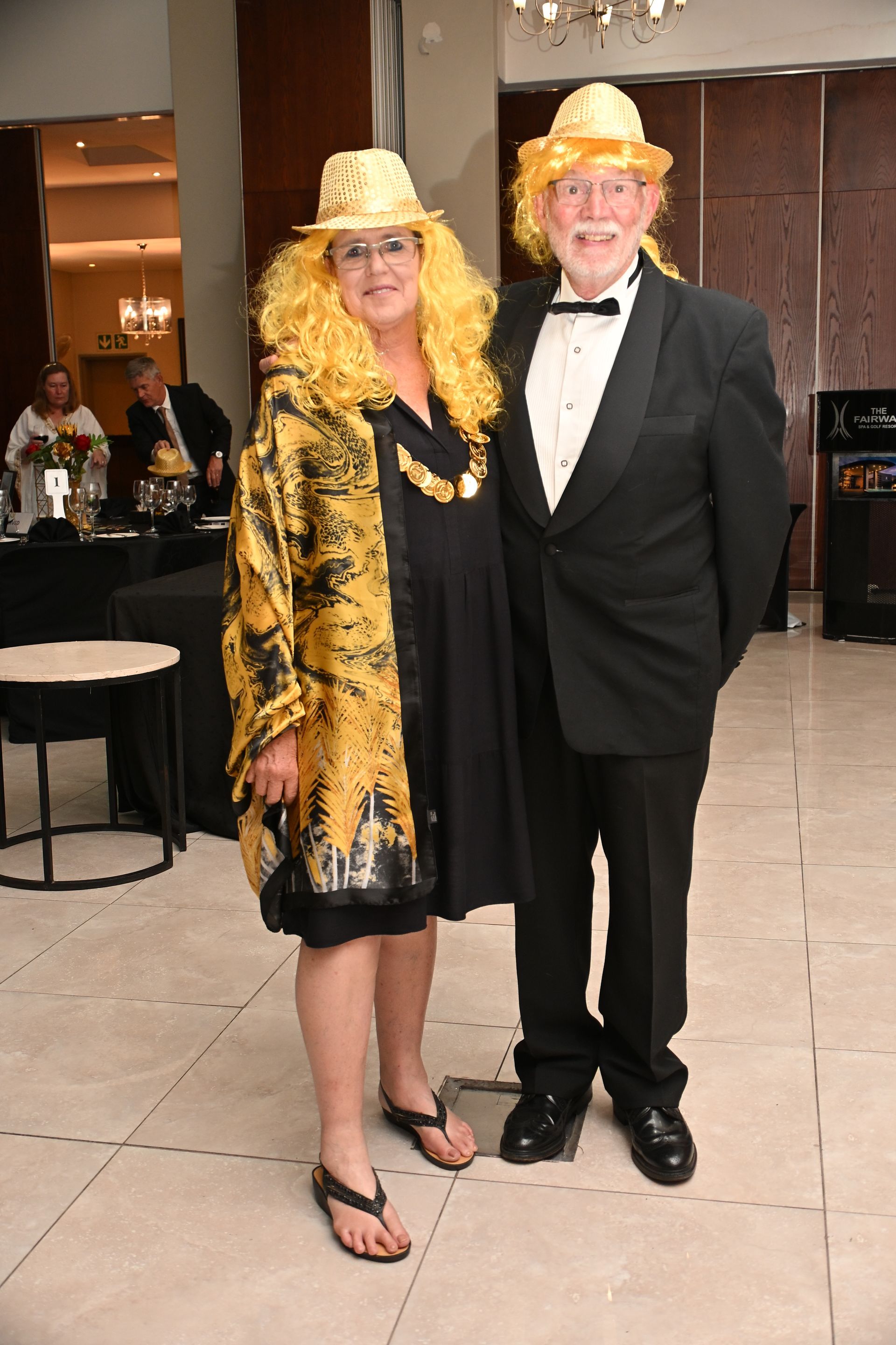 Two people in black tie and yellow hats standing together at an indoor event
