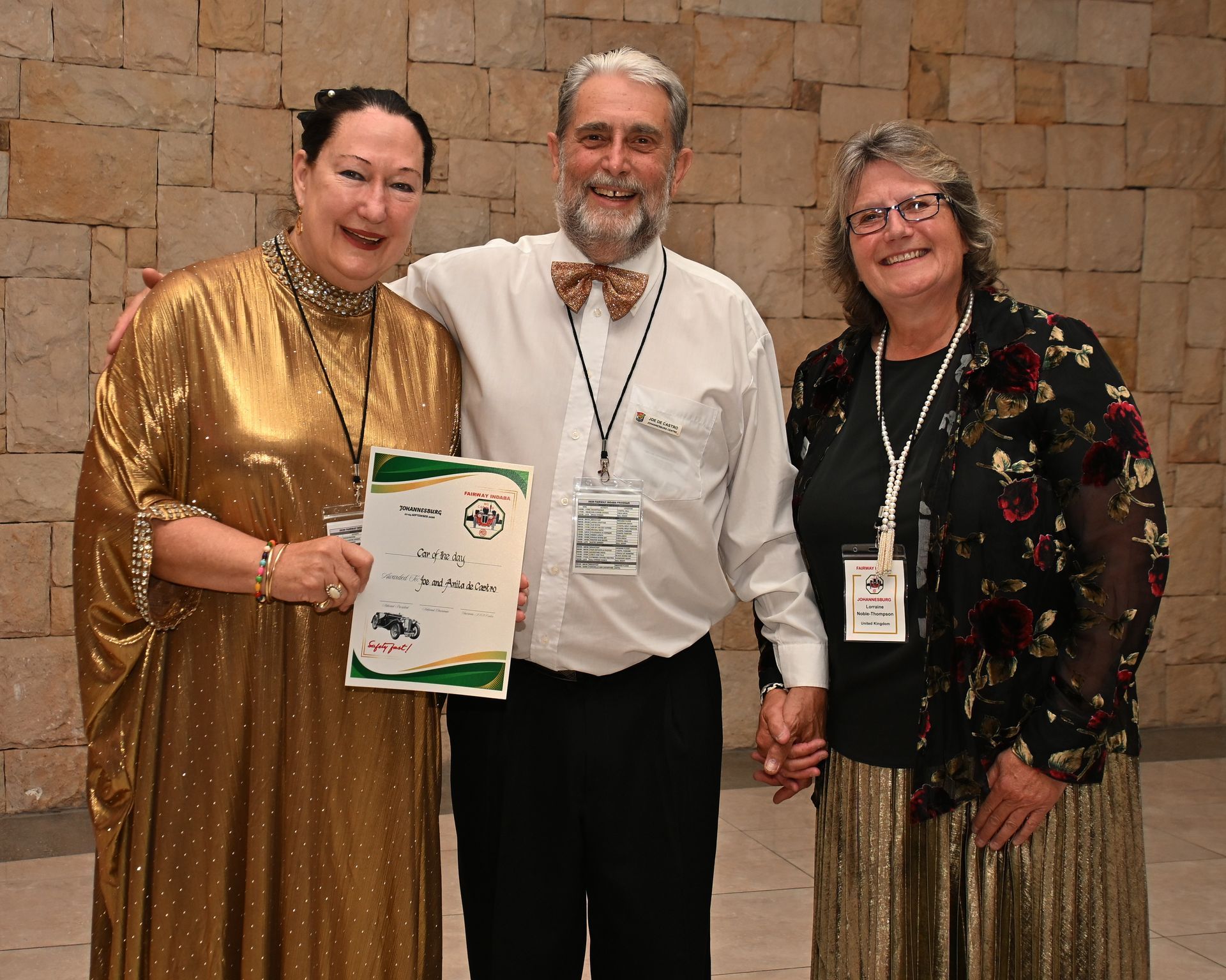 Three people standing together indoors, holding a certificate, smiling at the camera.