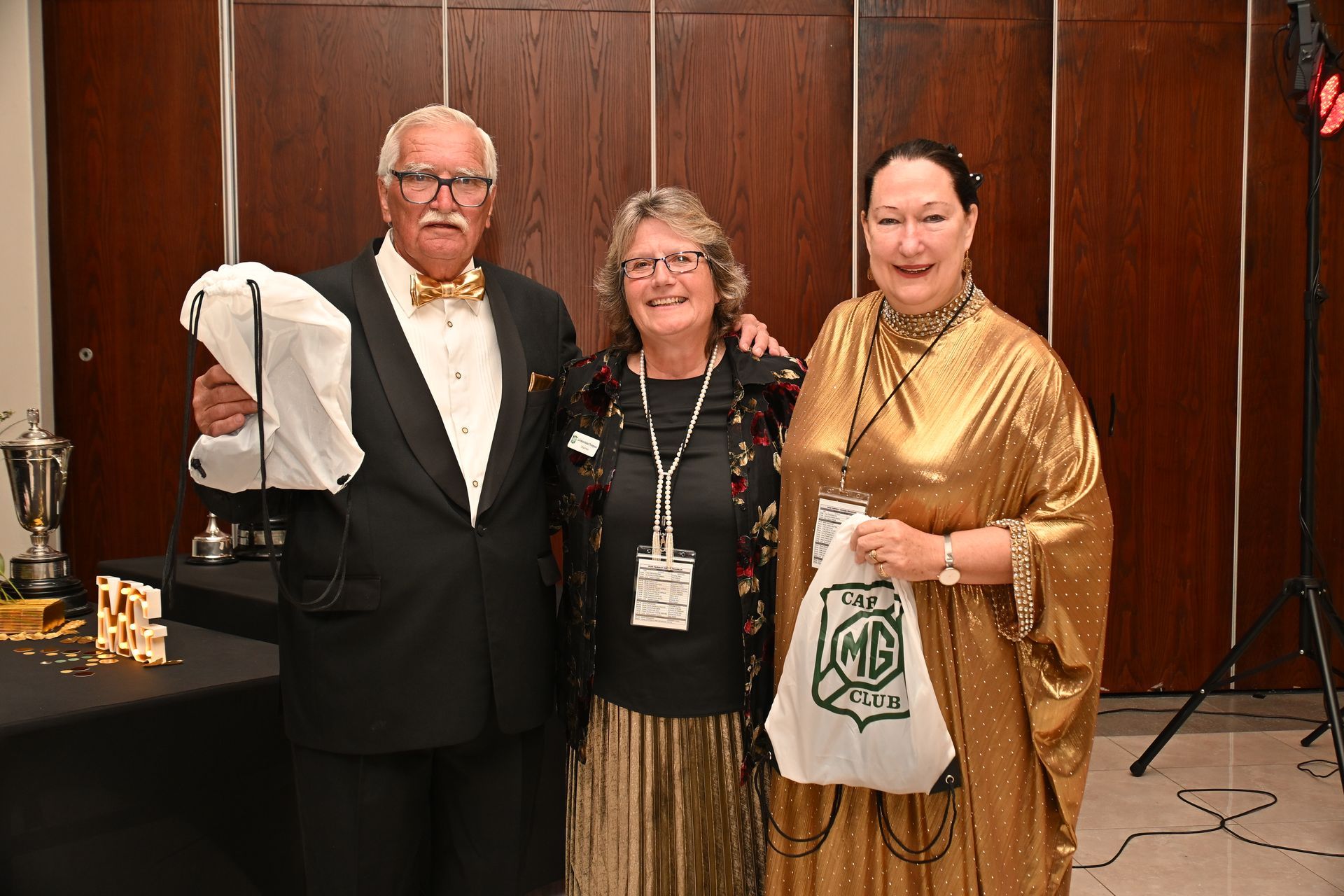 Three people posing at an indoor event, holding tote bags and wearing name badges