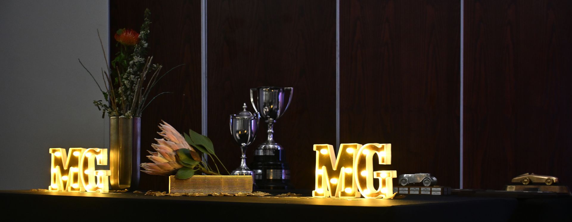 Lit “LOVE” letters on a banquet table with a trophy centerpiece and floral decor against a dark backdrop
