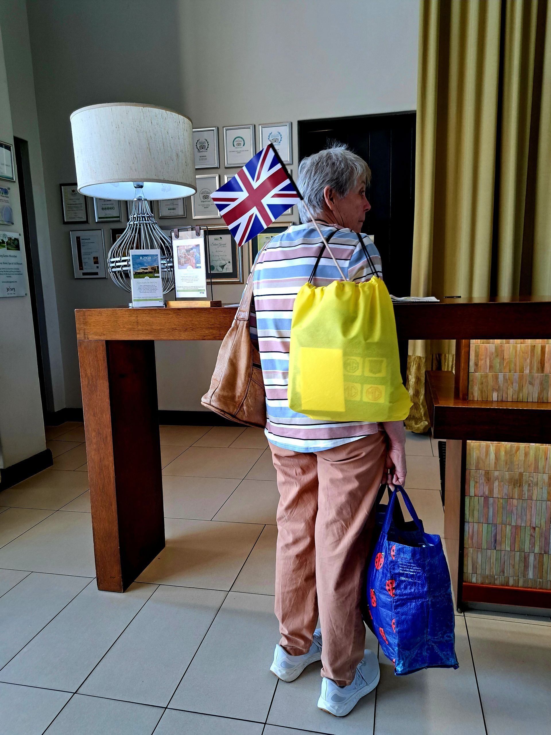Person with shopping bags stands at a reception desk in a tiled lobby.