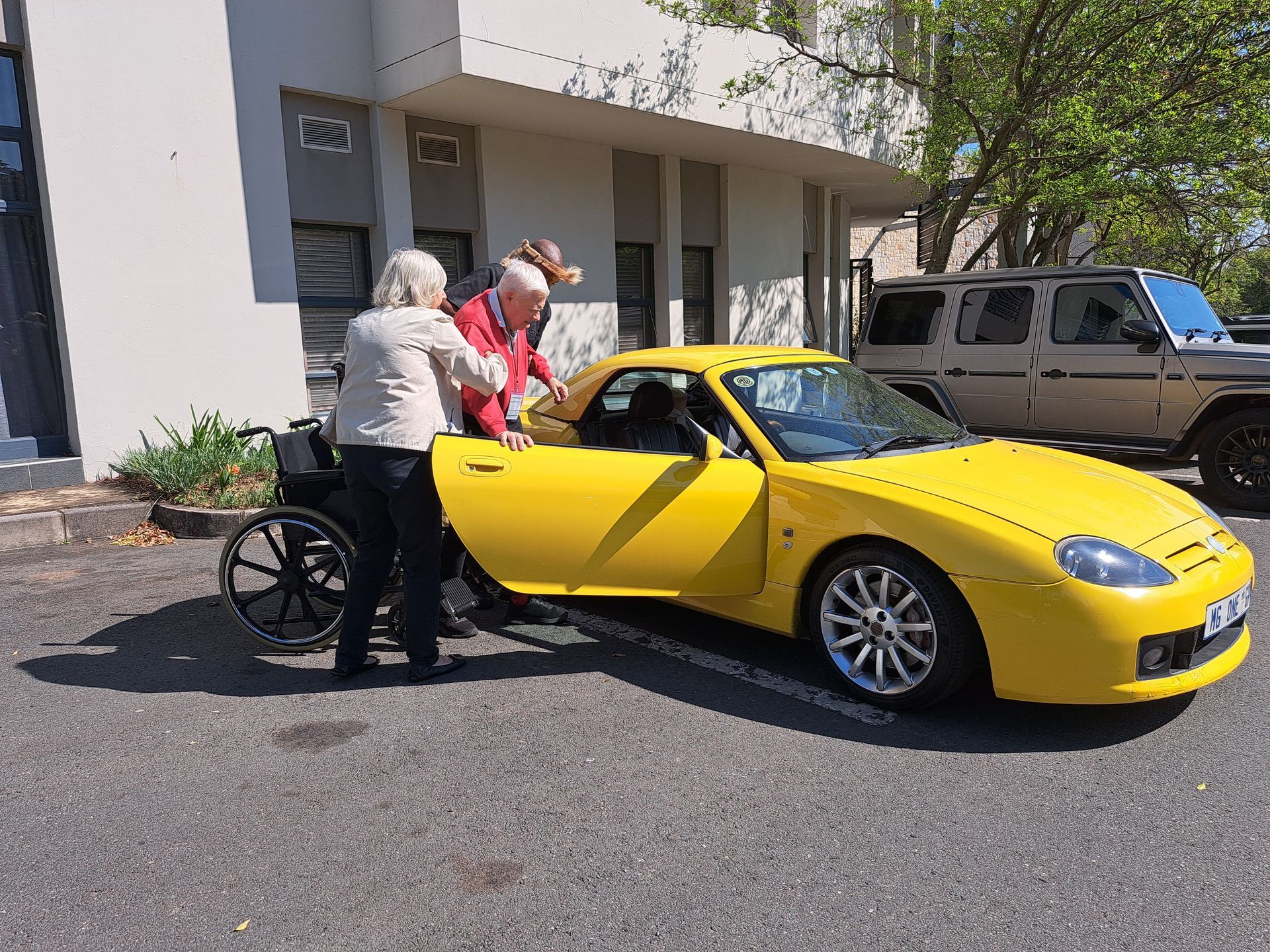Two people loading items into a yellow sports car outside a building