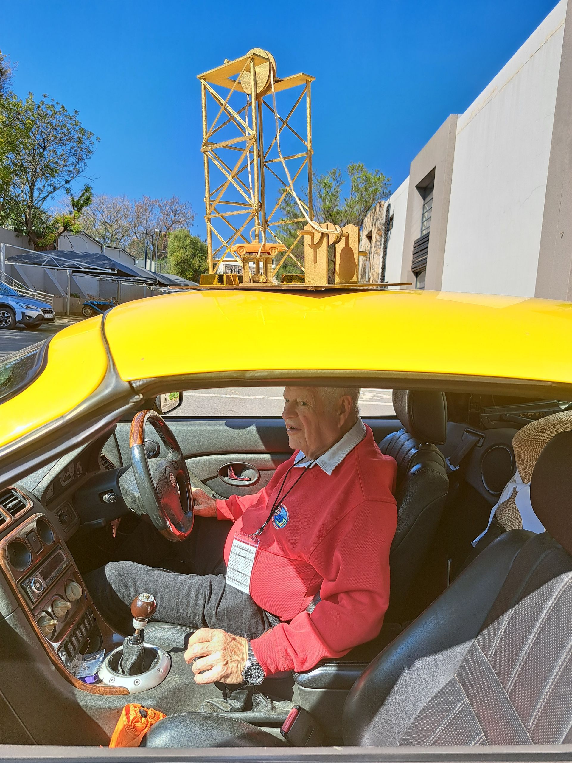 Person seated in a yellow sports car, smiling, with a roller coaster tower in the background
