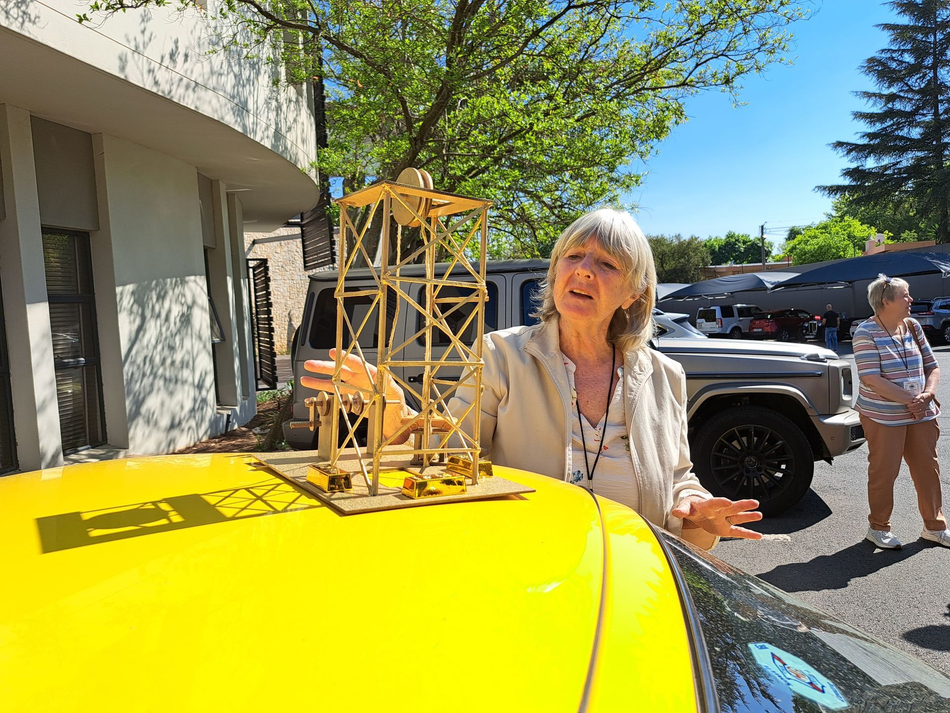 Woman beside bright yellow car with a small wooden tower model on the hood outdoors