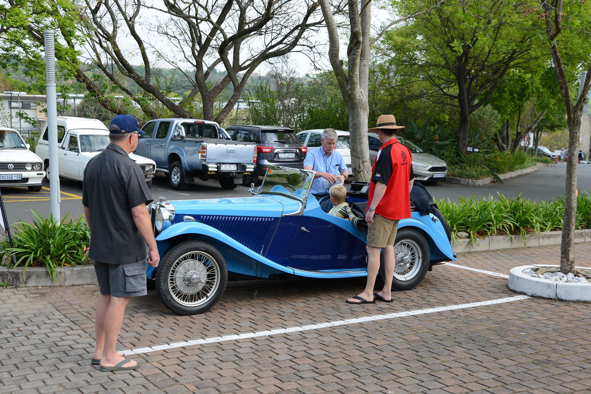 Three people standing around a blue vintage car in a parking lot