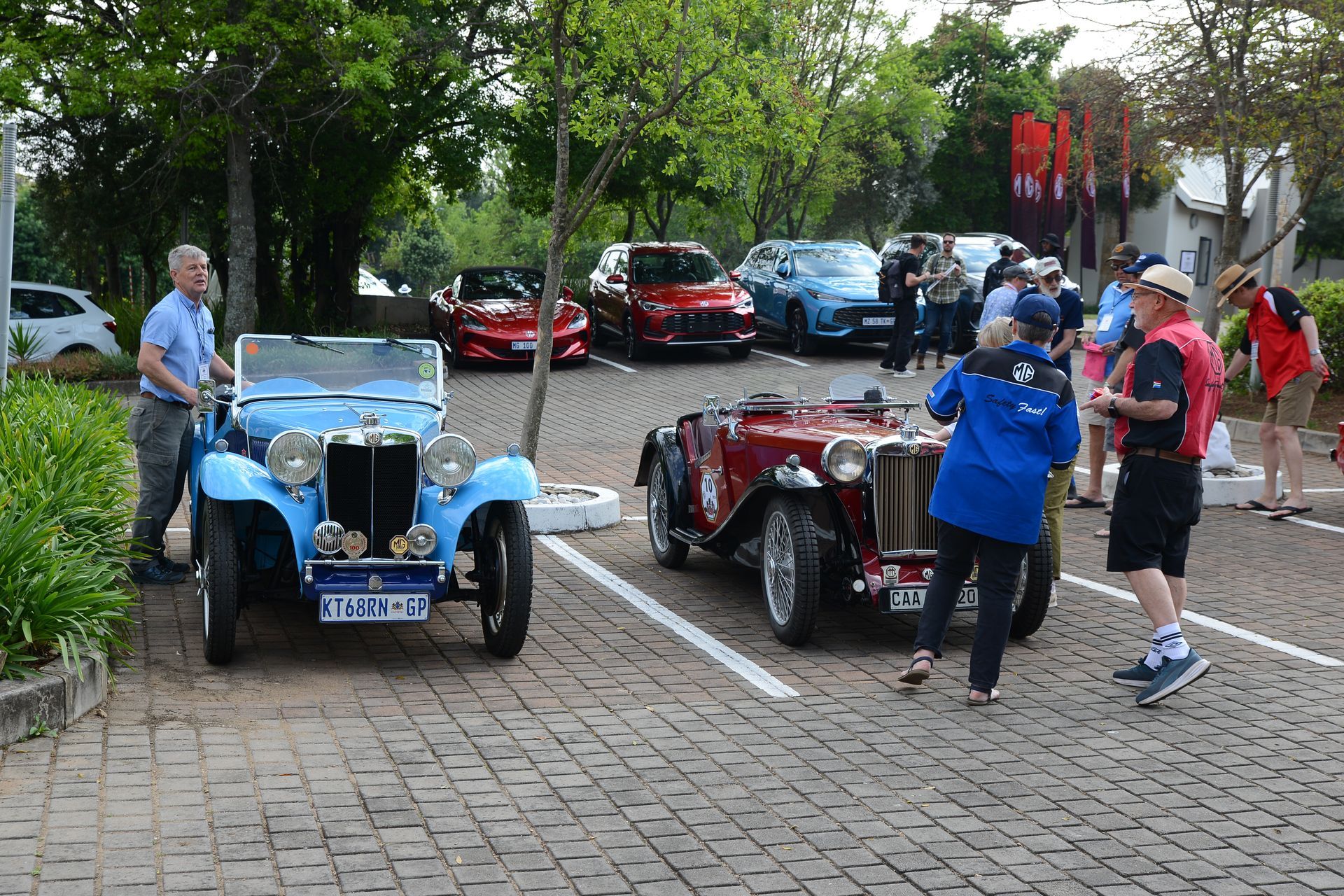 Vintage cars parked on a cobblestone street with people standing nearby outdoors