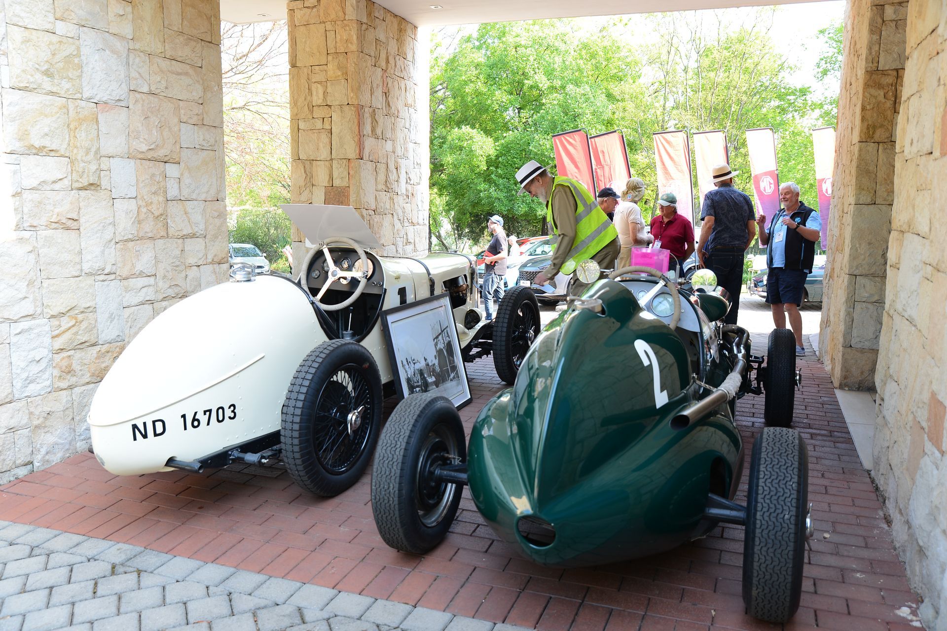 Two vintage race cars, white and green, parked under a stone archway