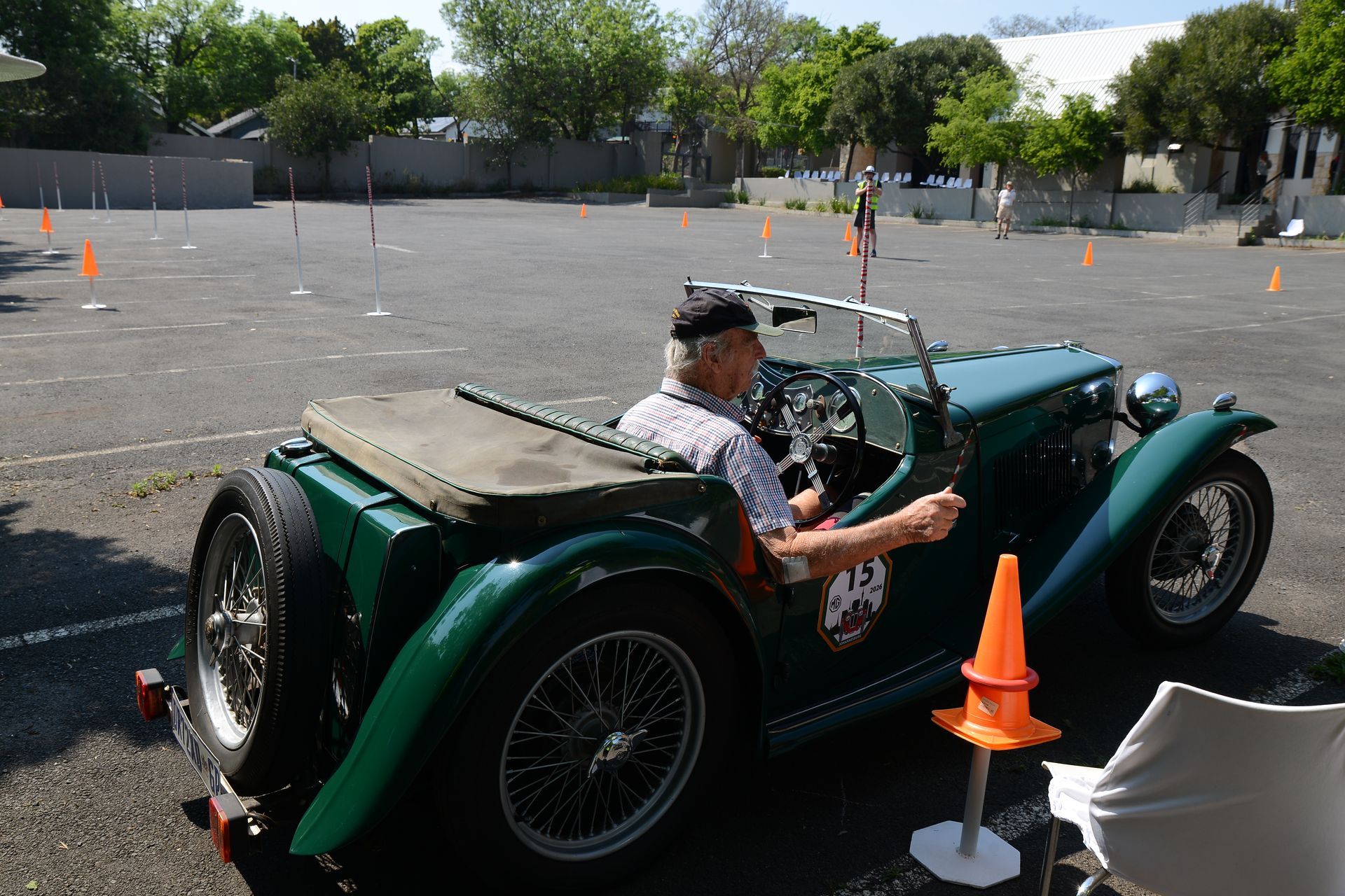 Green vintage roadster at an outdoor autocross course, with driver and orange cones nearby