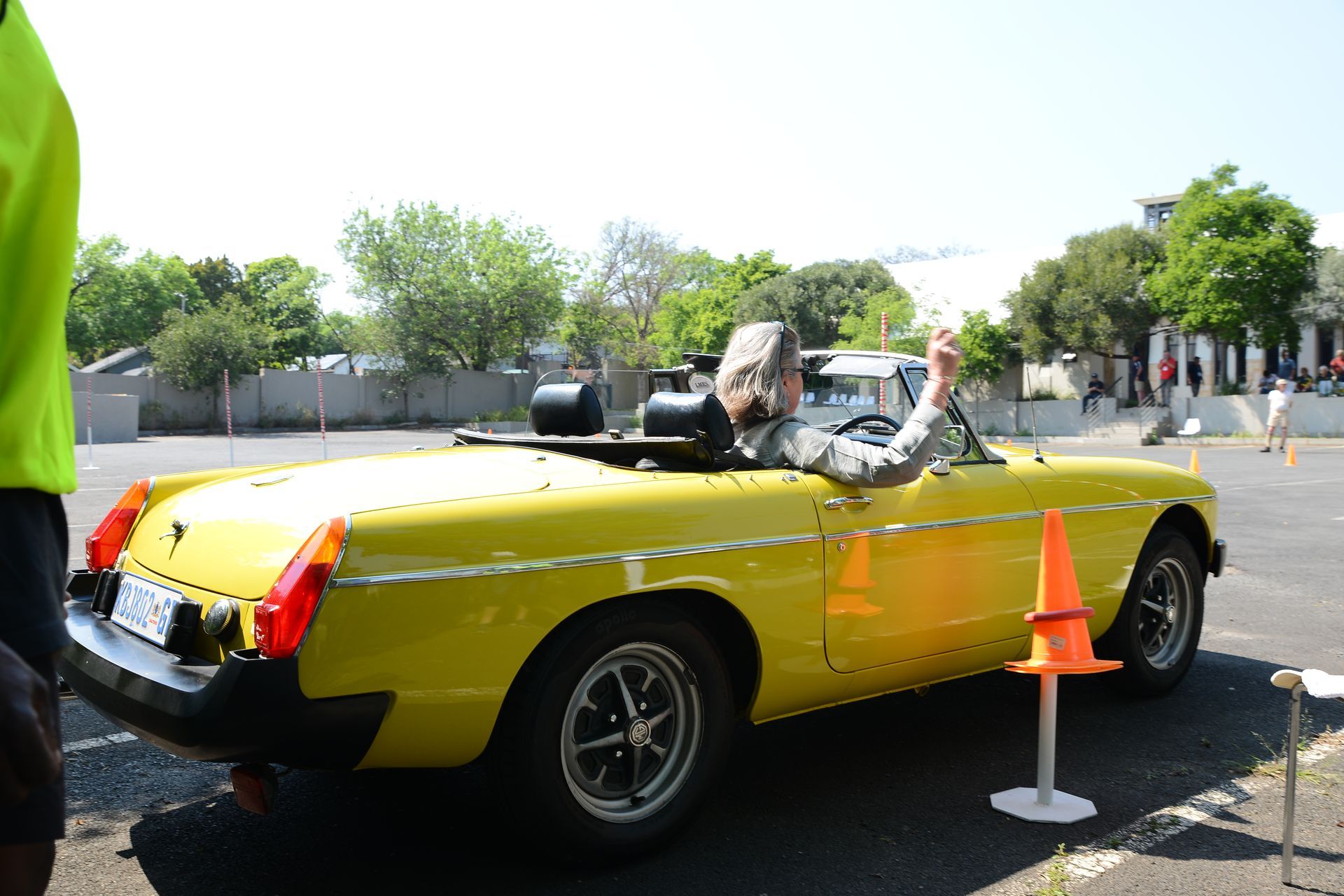 Yellow convertible with a driver, parked at a roadside event beside orange traffic cones