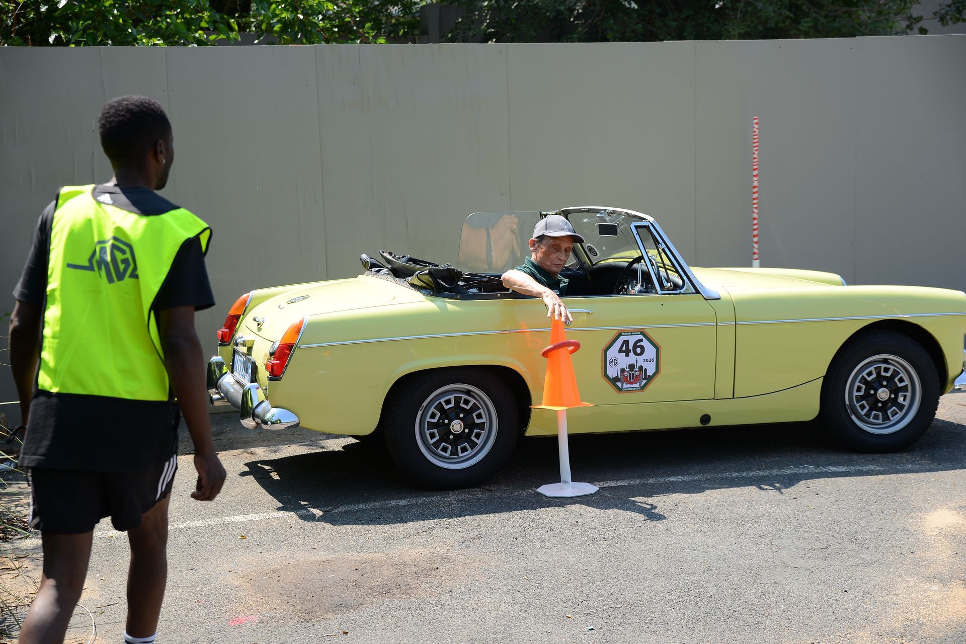Yellow convertible with driver stopped by race marshal in neon vest on a road course￼