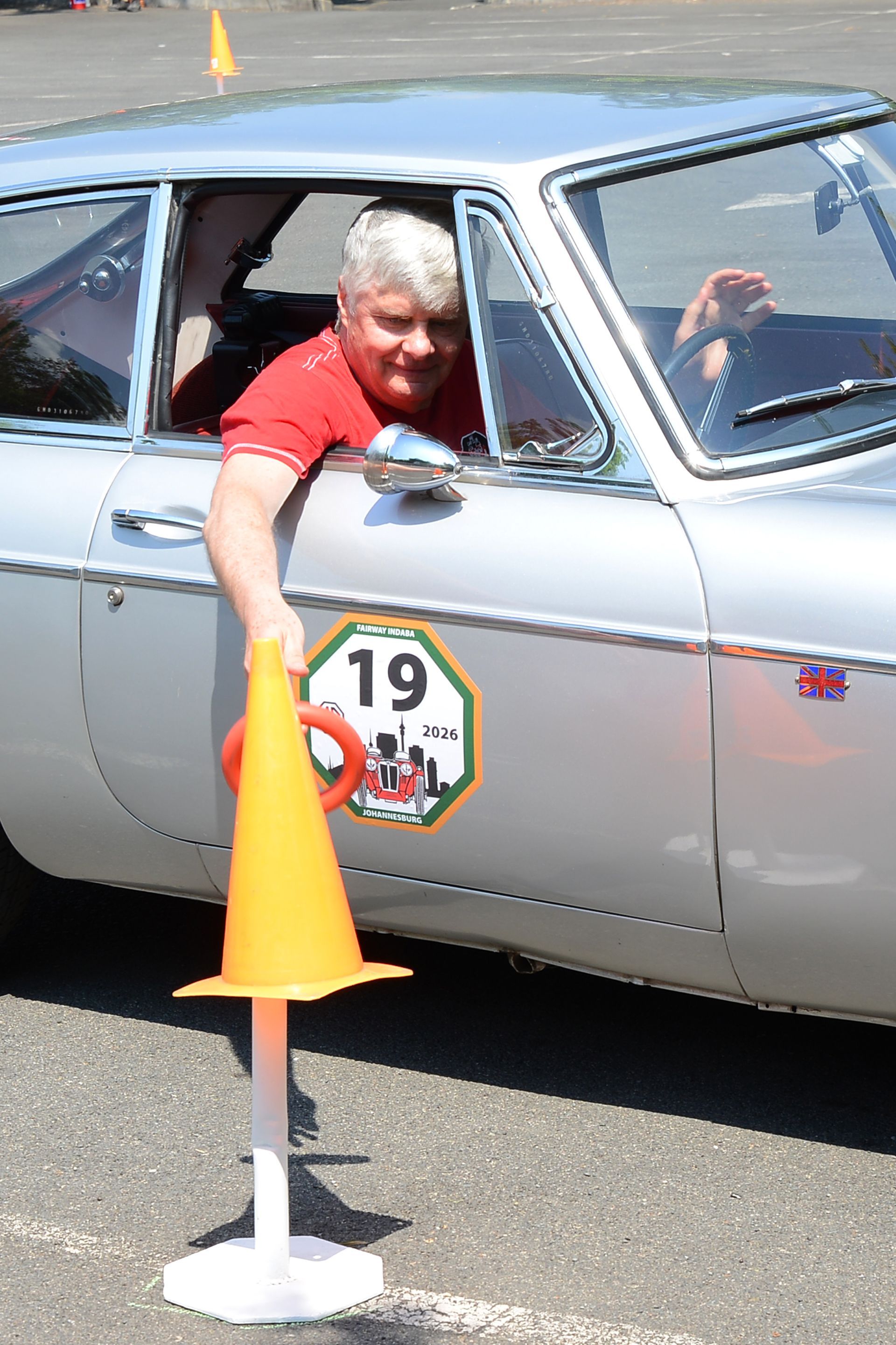 Driver reaching from a silver car through a cone in a parking lot competition
