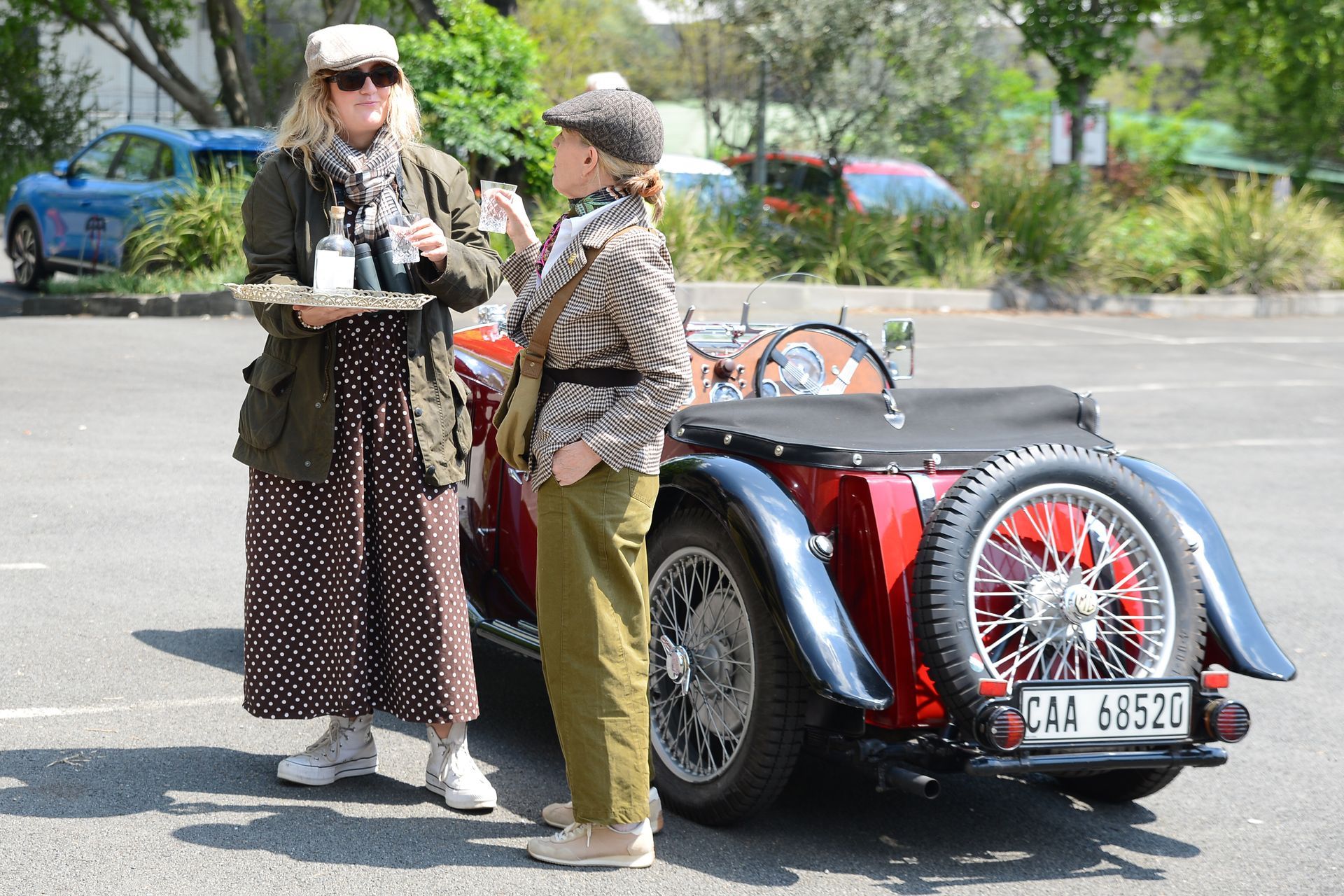 Two people standing beside a red vintage car in a parking lot