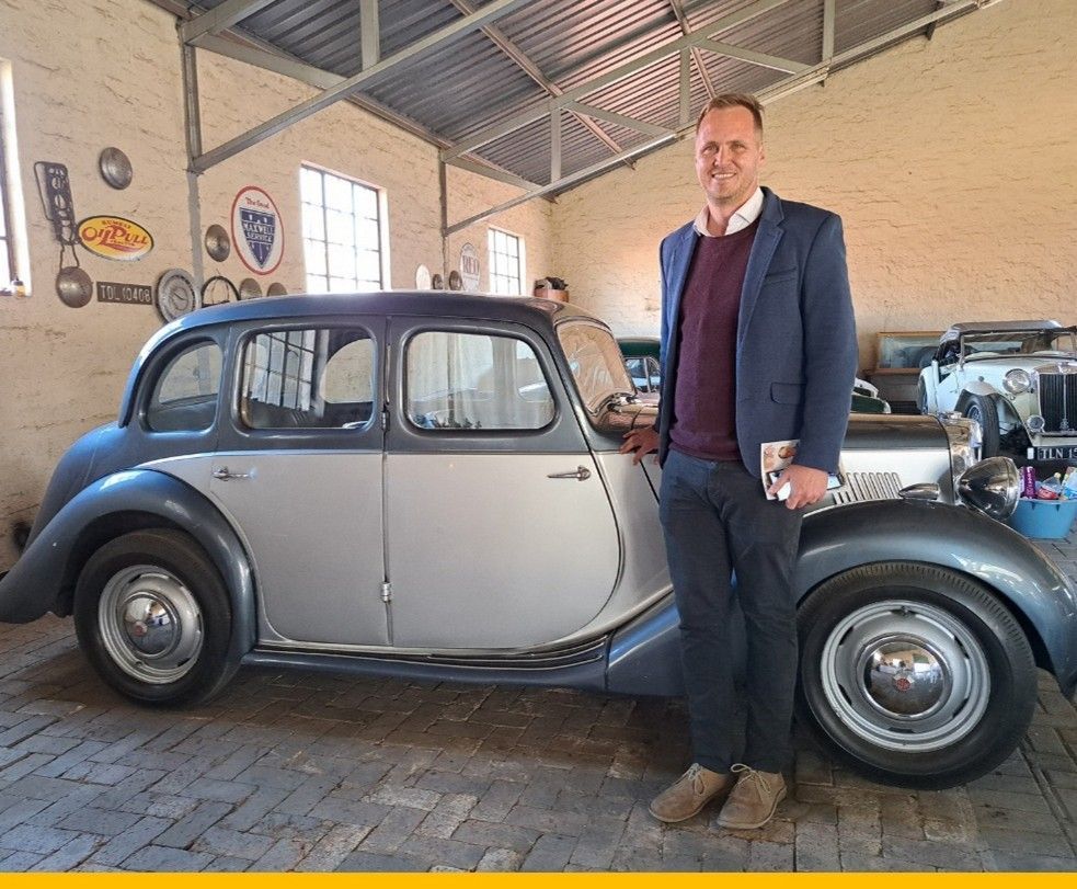 Man stands next to a classic silver and blue car in a garage.