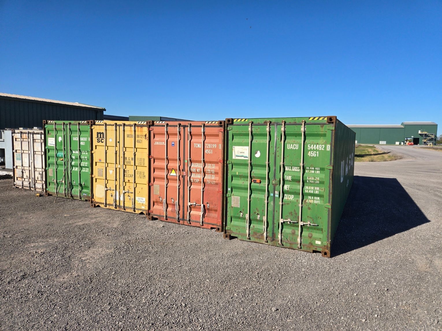 Several colorful shipping containers on a gravel surface under a blue sky.