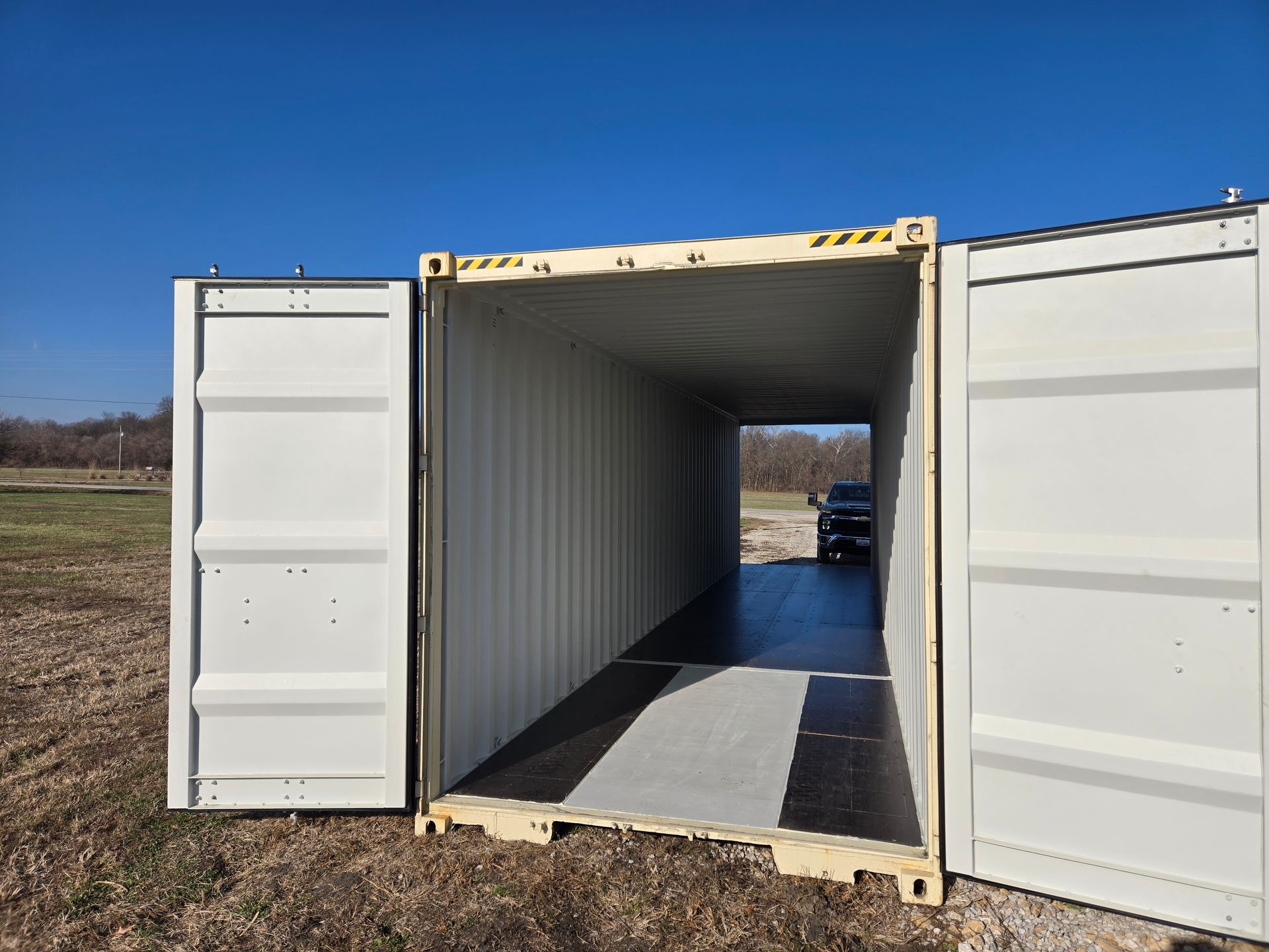 Open beige shipping container with doors open, revealing interior and a vehicle visible in the distance.