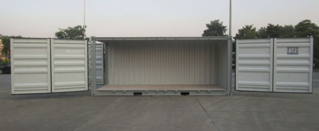 An open, empty white shipping container with doors spread wide in an outdoor setting.