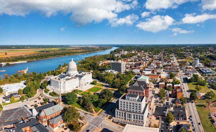 Aerial view of Jefferson City, Missouri, with the state capitol building near the Missouri River under a blue sky.