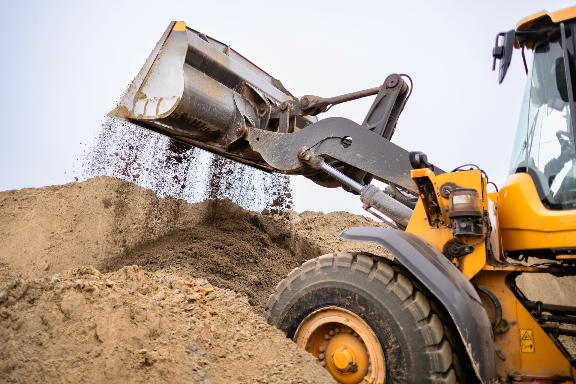 Front end loader dumping sand from raised bucket at a construction site.