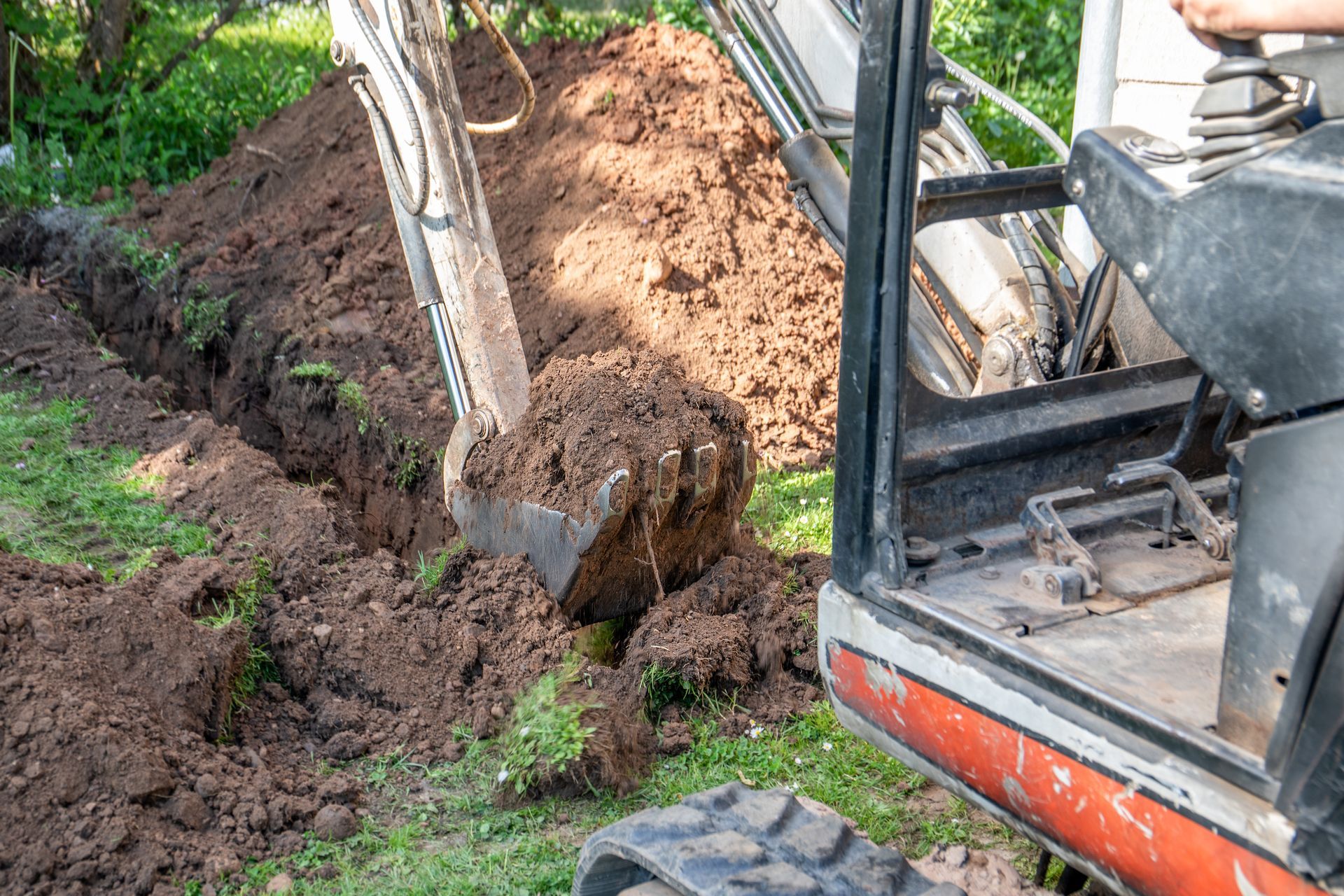 Mini excavator digging a narrow trench in soil with bucket scooping earth outdoors. Mini excavator digging a narrow trench in soil with bucket scooping earth outdoors.