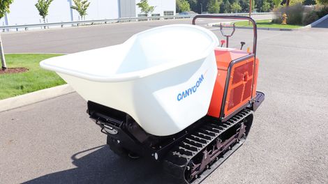 Orange and black tracked dumper with a white tub on asphalt.