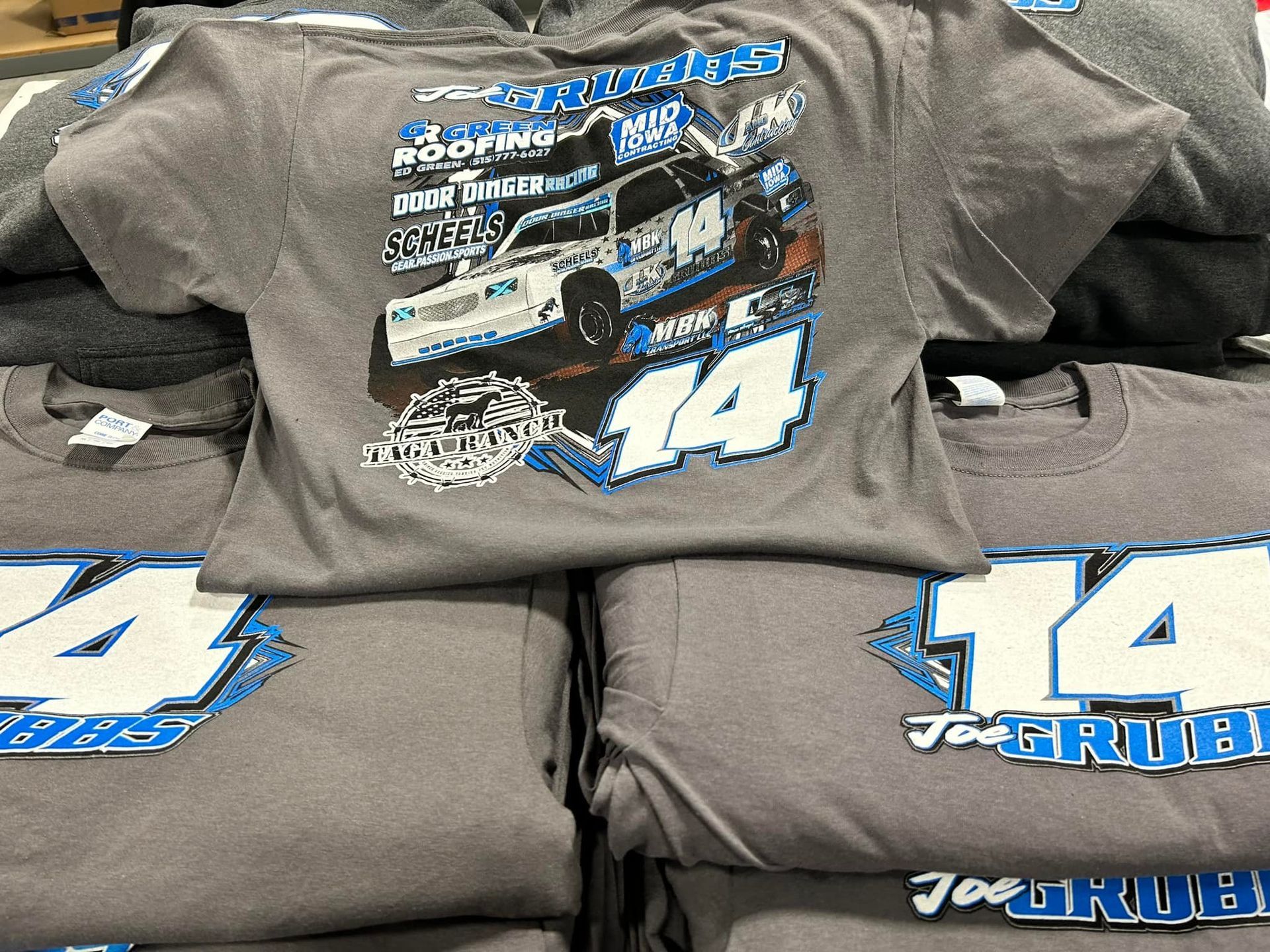 A stack of gray T-shirts featuring a race car graphic and the number 14 with the name Joe Grubb.