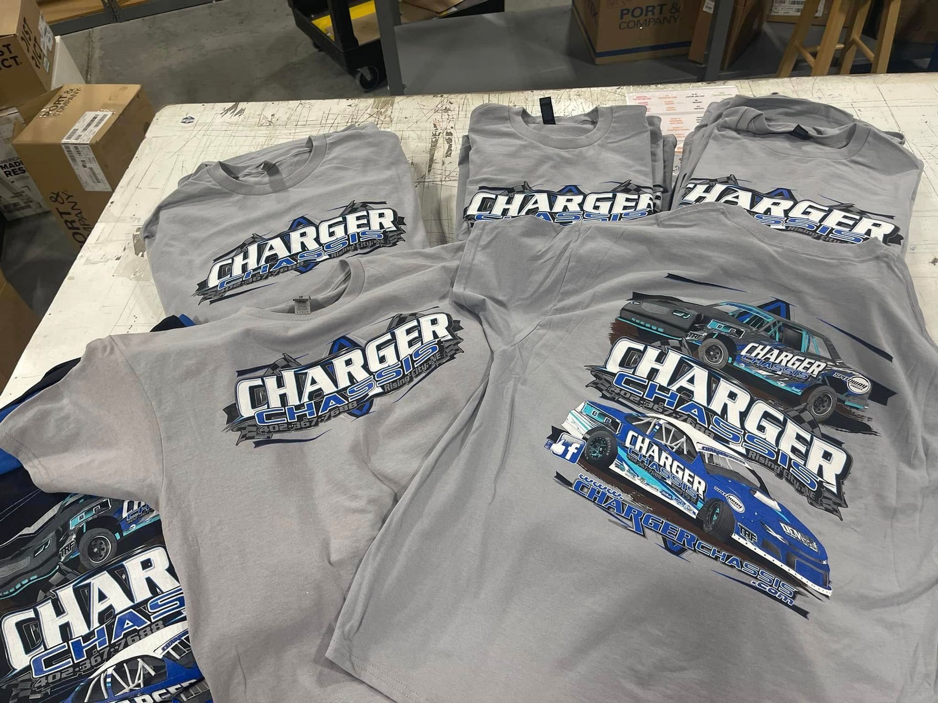 Several gray t-shirts featuring a blue race car graphic with the word