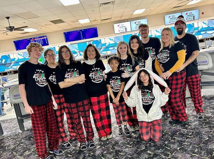 A group of people wearing matching black shirts and red plaid pants pose for a photo at a bowling alley.
