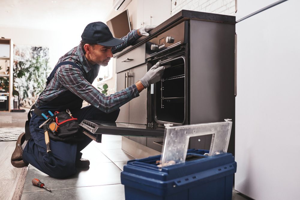 Electrician Examining Oven With Screwdriver In Kitchen — PRO Solar & Electrical In Port Stephens, NSW